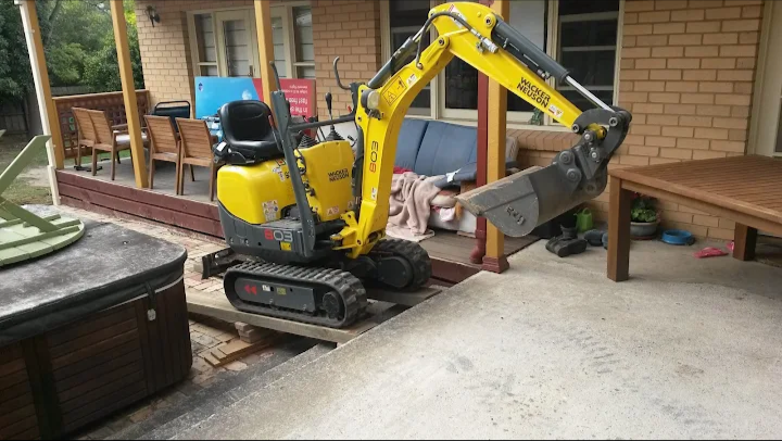 Small yellow and black mini excavator on a concrete patio.