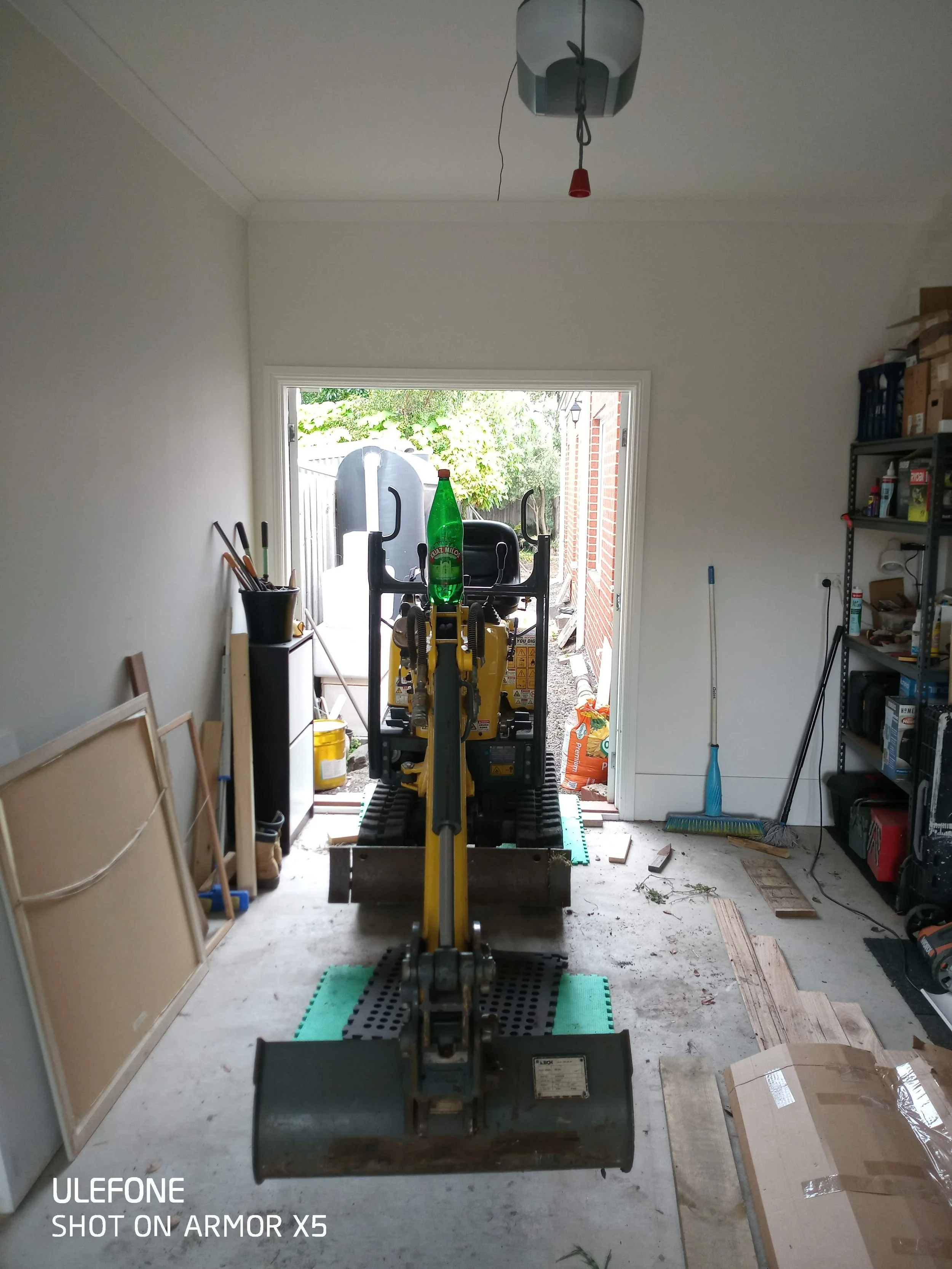 Construction tools and equipment in a garage or workshop, with a small excavator or skid steer loader near the open garage door.