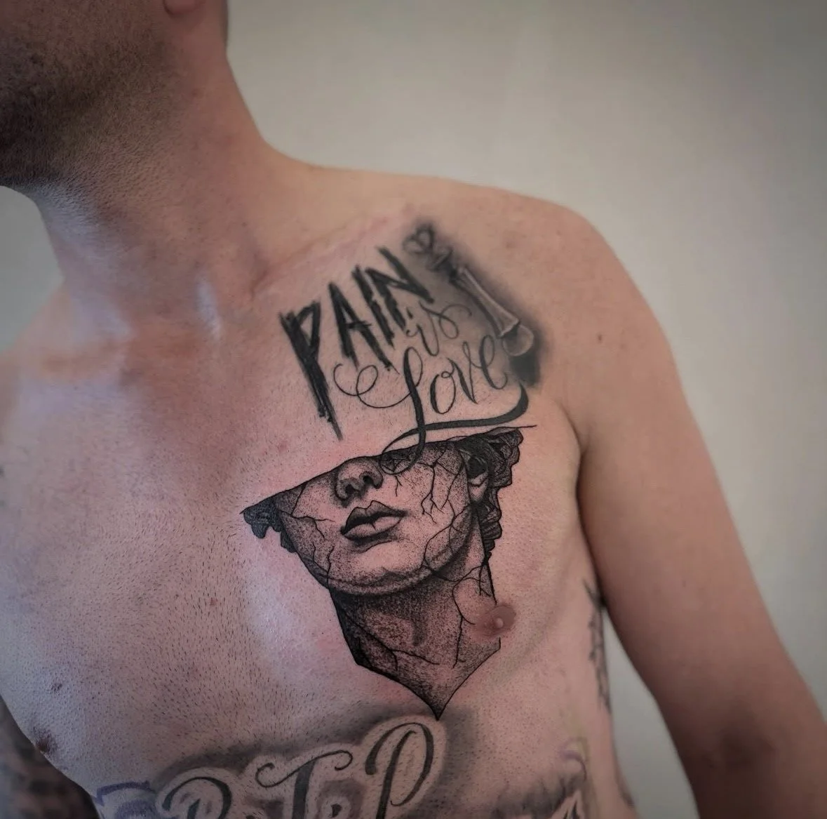 Tattoo on man's chest featuring the face of a woman with cracks, the words "Pain to Love," and decorative elements.