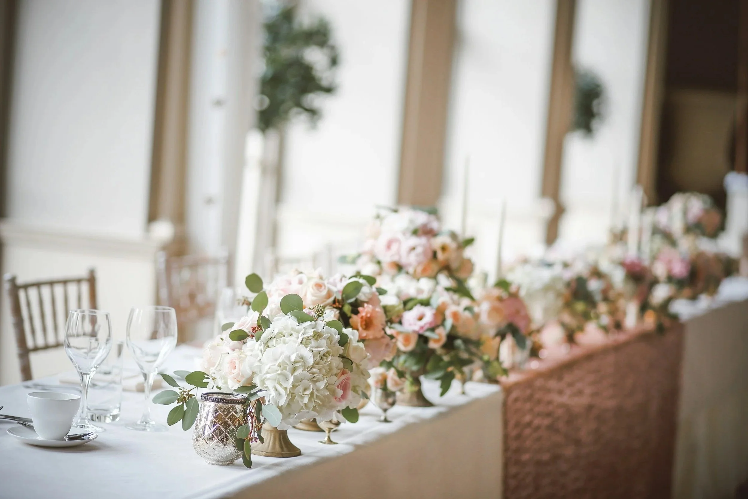 A long trestle table set for a wedding with pink and white flowers.