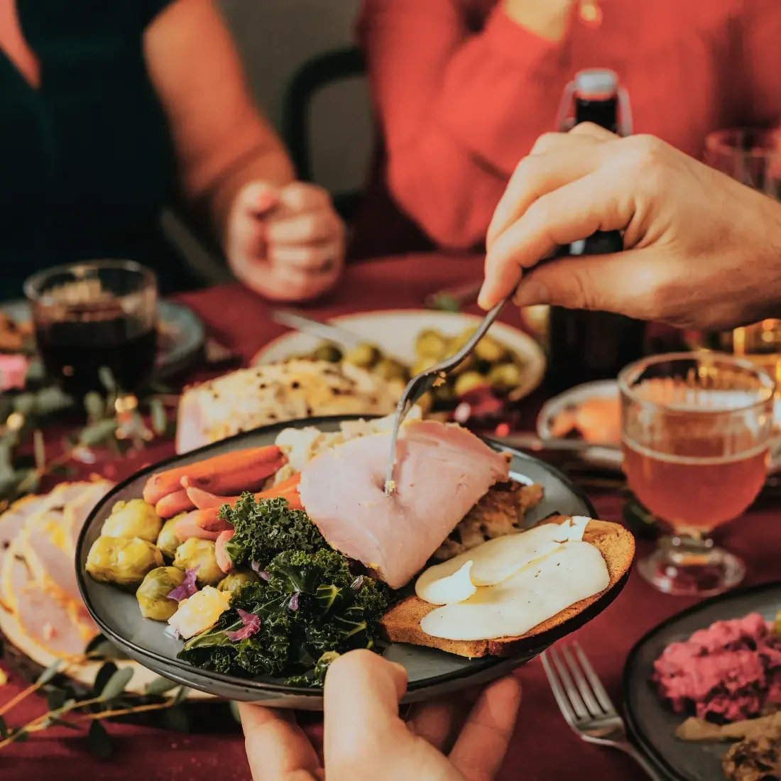 Plates of Christmas food in the foreground and a blurred, busy Christmas table behind.