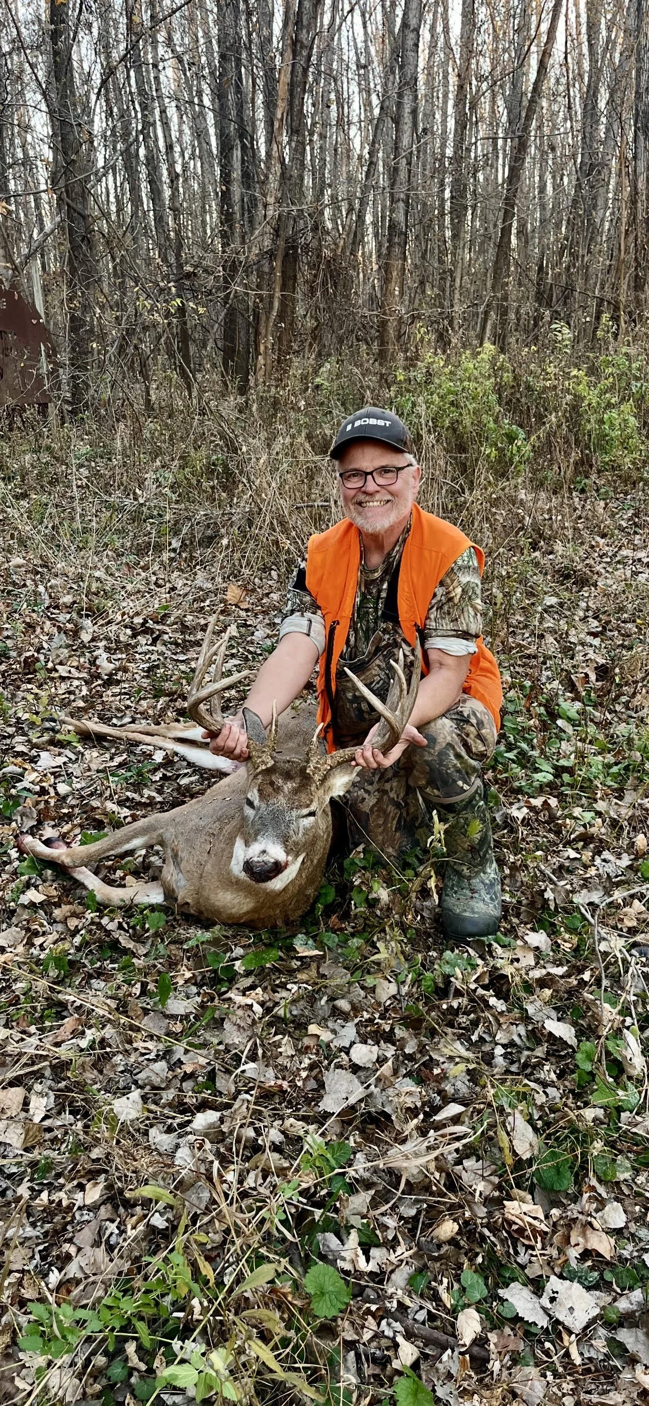 Hunter wearing hunter orange kneels beside a harvested whitetail buck on a wooded trail at Tegridy Outdoors in Missouri.