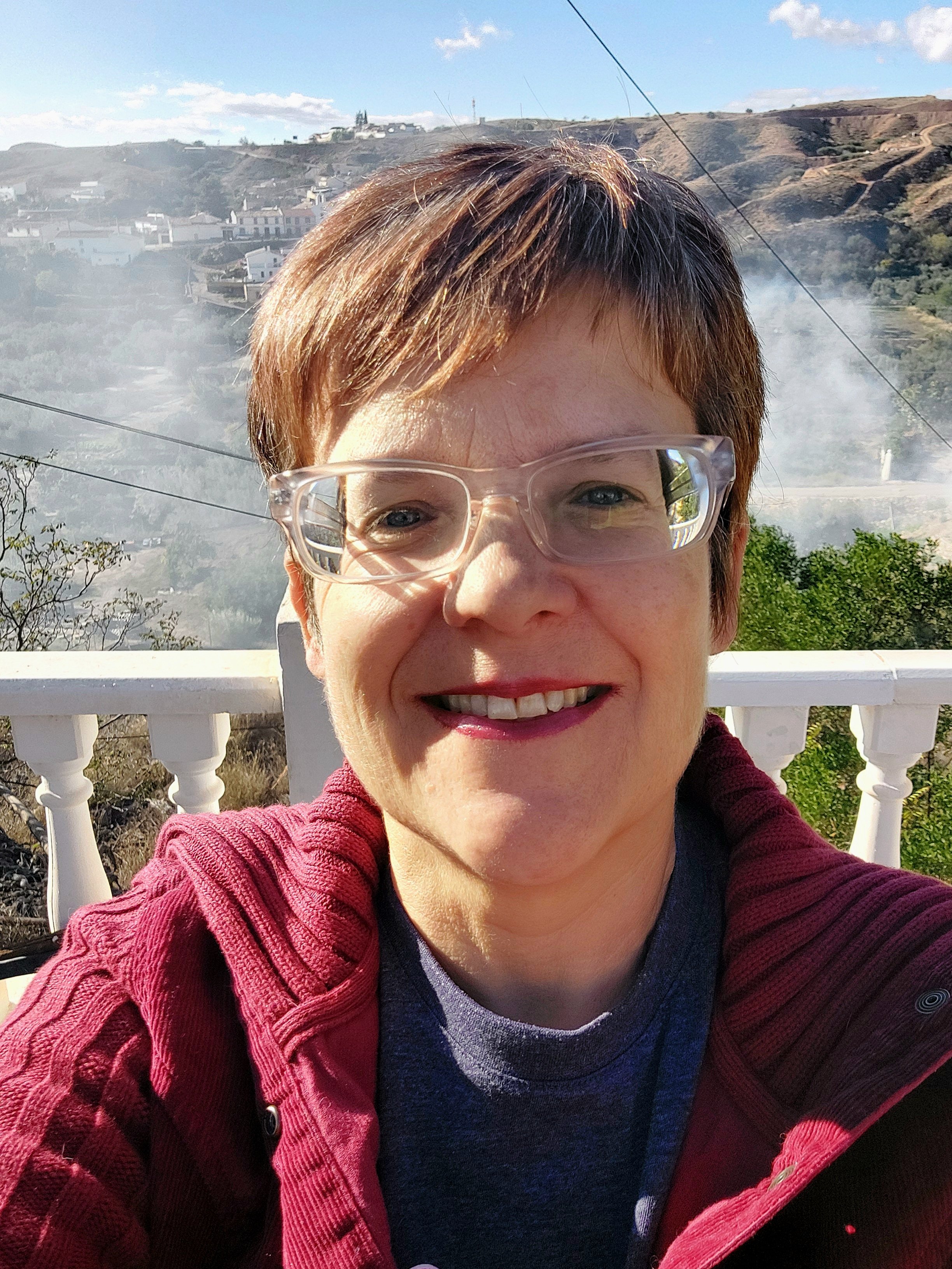 Picture of Helen the founder smiling at the camera whilst sat outside with smoke billowing behind her.