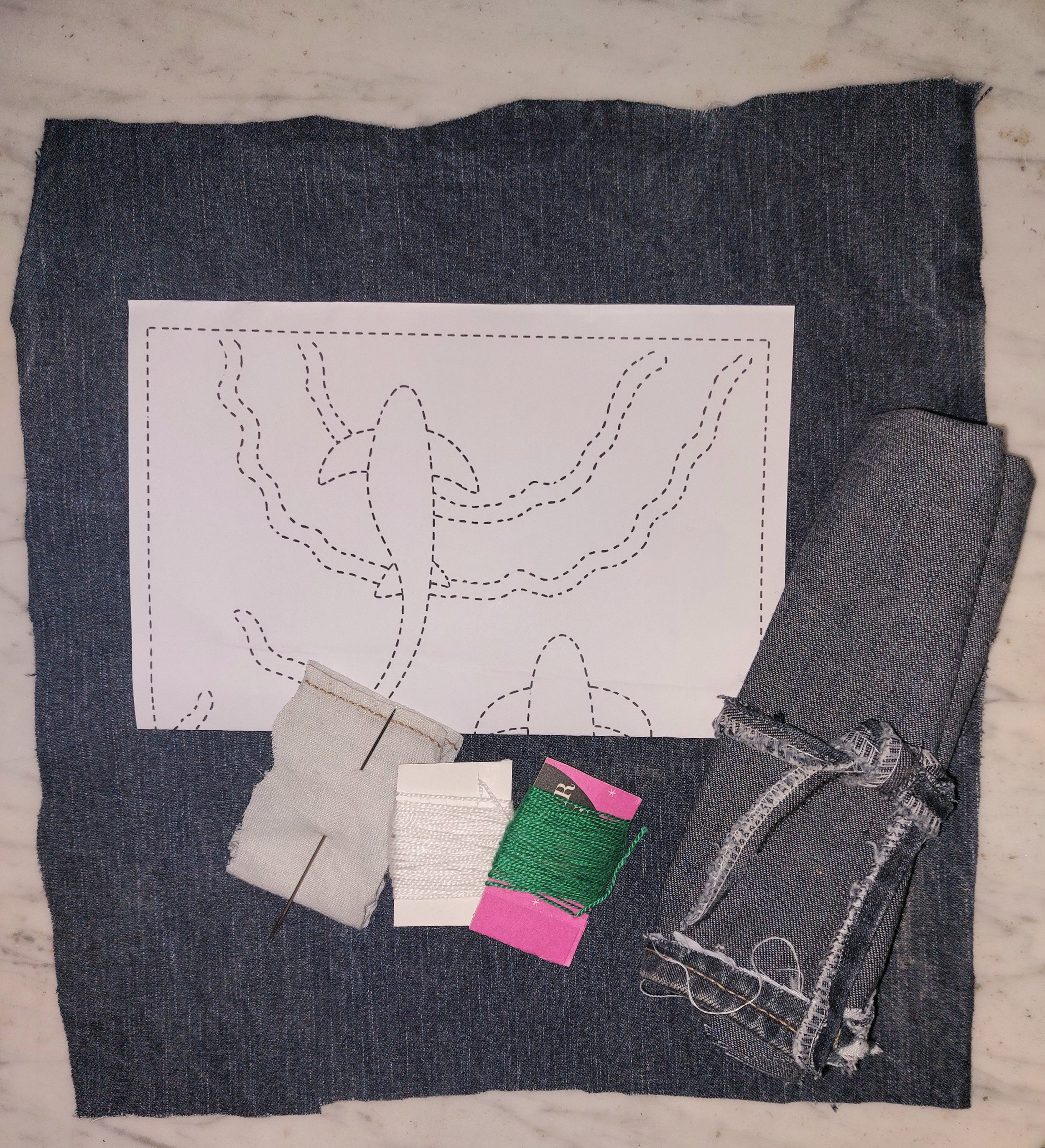 articles of the Boro kit laid out on a marble table top.  Items include piece of denim, pattern, threads, needle and example of how it comes packaged