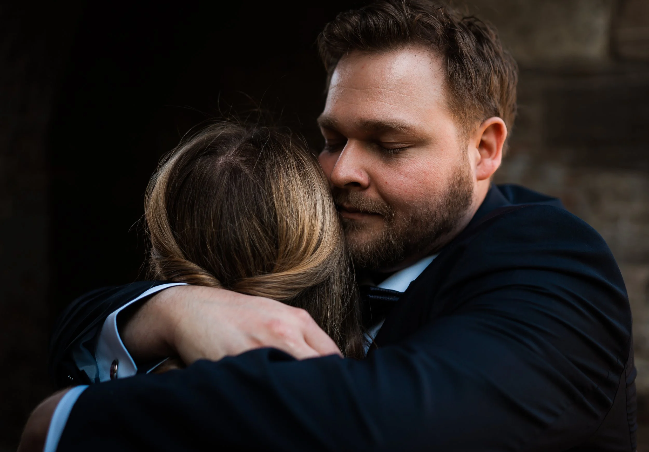 Ein Mann und eine Frau umarmen sich liebevoll, sie haben die Augen geschlossen, in einem dunklen Hintergrund.