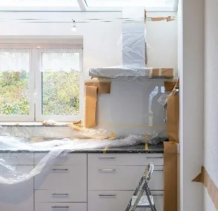 Kuvassa on keittiö, joka on parhaillaan uudistuksen tai maalausprojektin alla. Maalausta varten laitettu suojia pinnoillle.