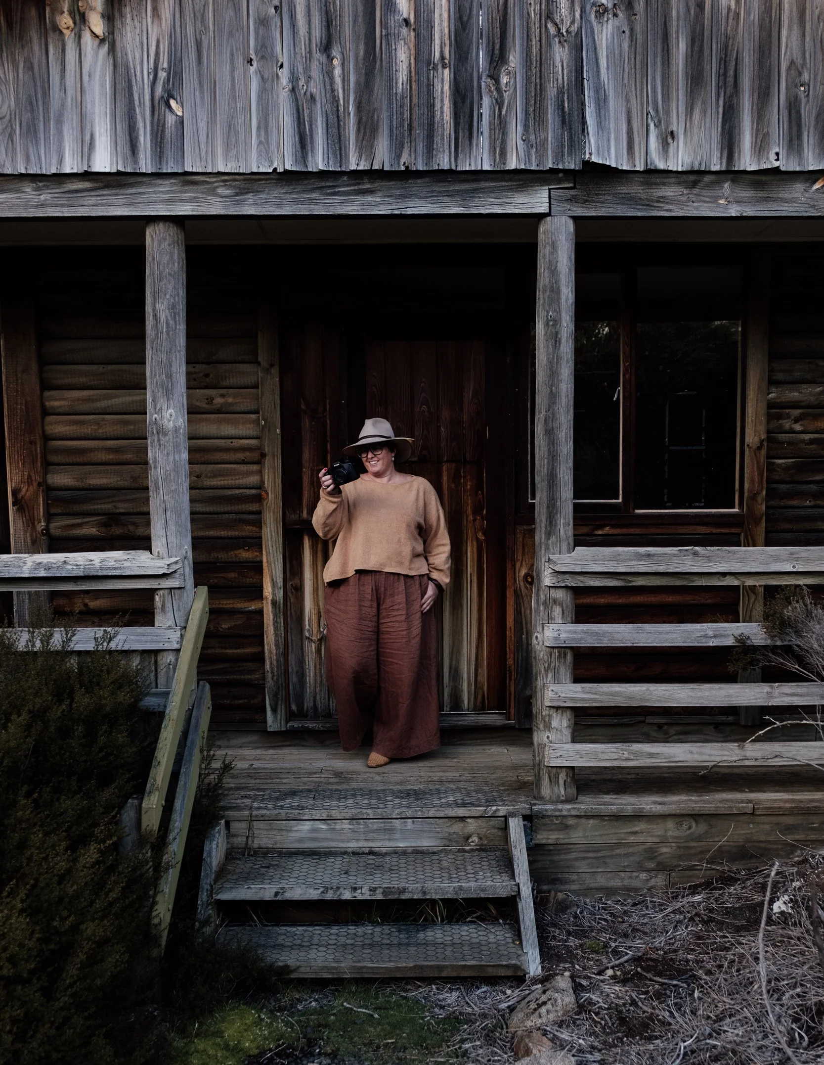 photographer standing on the porch of a wooden house holding a camera.