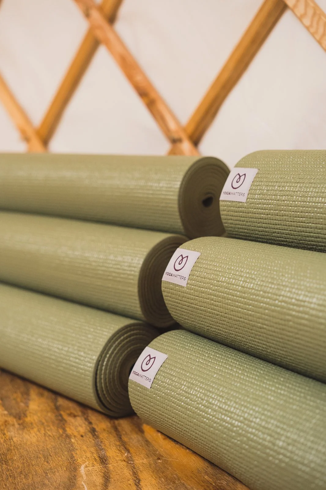 An image of olive green yoga mats neatly rolled and stacked inside of the yurt.