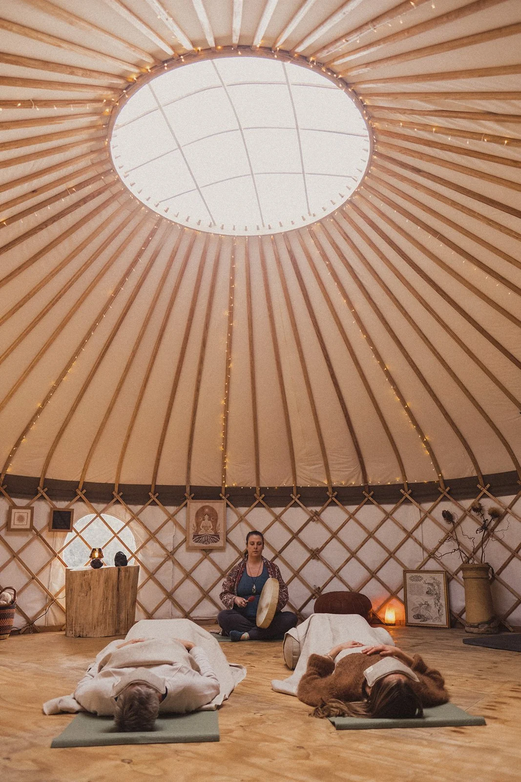 Two people lying on yoga mats during a  shamanic ceremony inside Whiteleaf Yurt with wooden interior and decorative items.