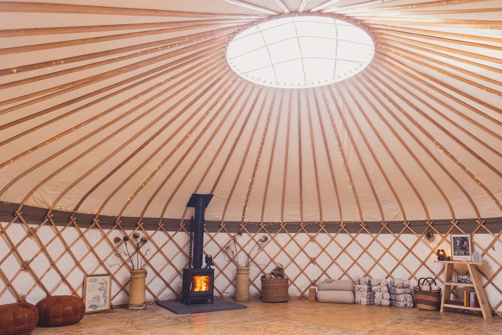 Wide view of the interior view of The Whiteleaf Yurt, with the woodburner alight, and equipment neatly stacked.