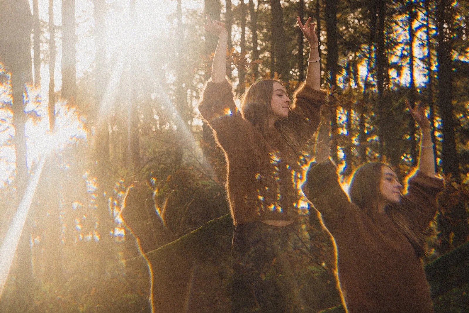 A double exposure image of a young women dancing outdoors in a forest with sunlight shining through trees, wearing a brown sweater.