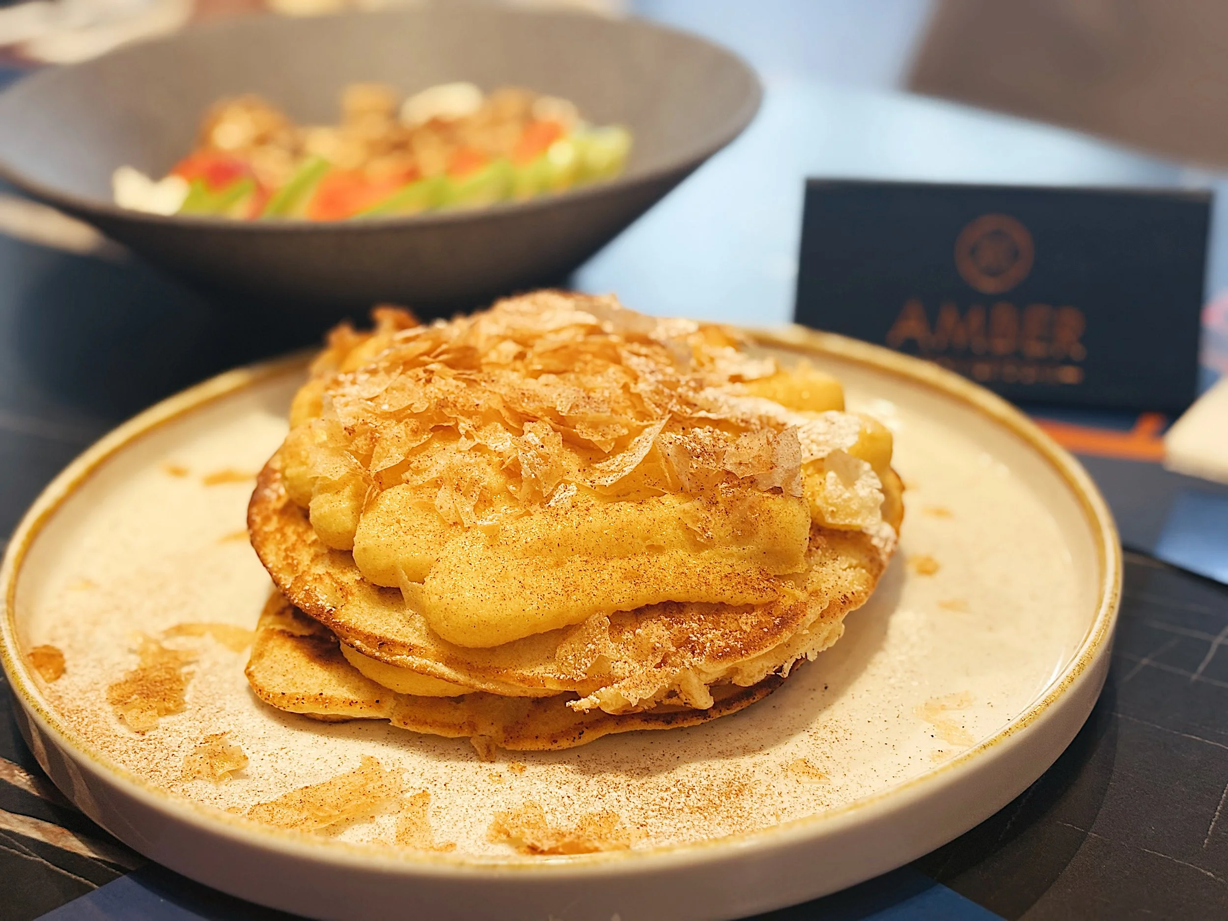 A dessert with layered pastry topped with apple slices, sliced almonds, and cinnamon, served on a white plate.