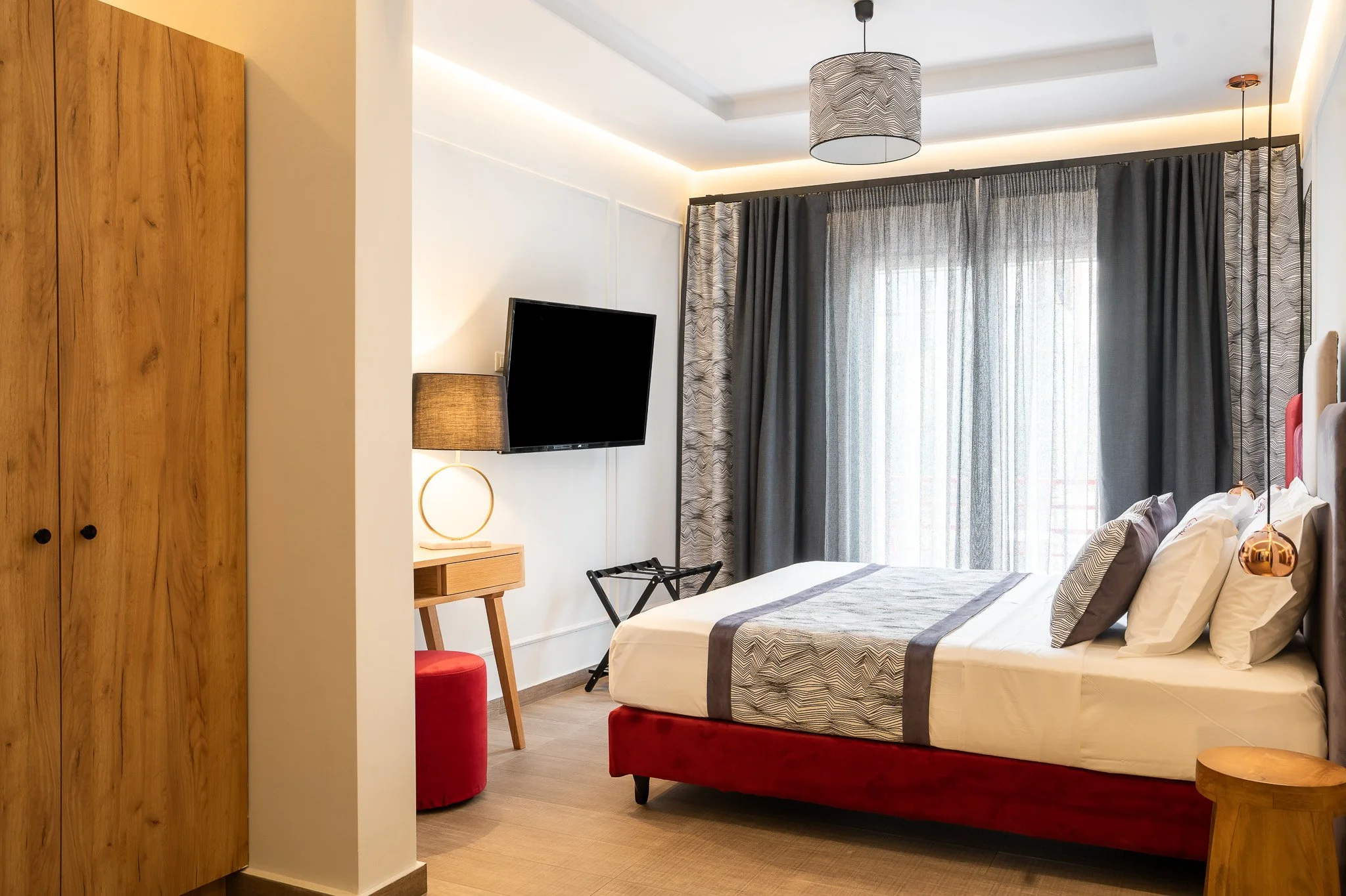 A modern hotel bedroom with a bed, curtains, wardrobe, and wall-mounted TV.