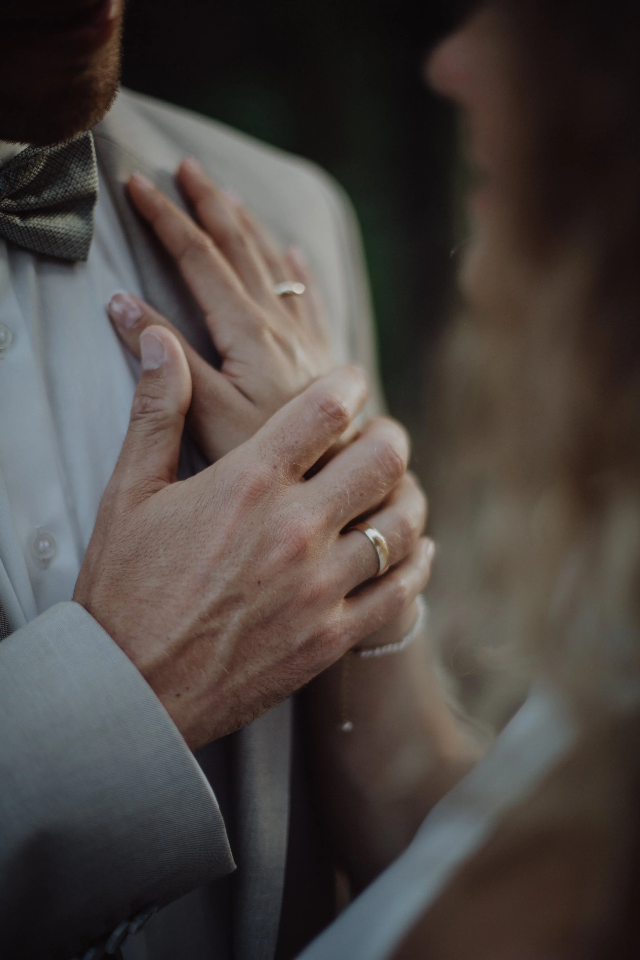Nahaufnahme eines Paares während einer Hochzeitszeremonie, die Hand des Mannes mit Ehering wird auf die Brust der Frau gelegt, beide in formeller Kleidung, emotionaler Moment.
