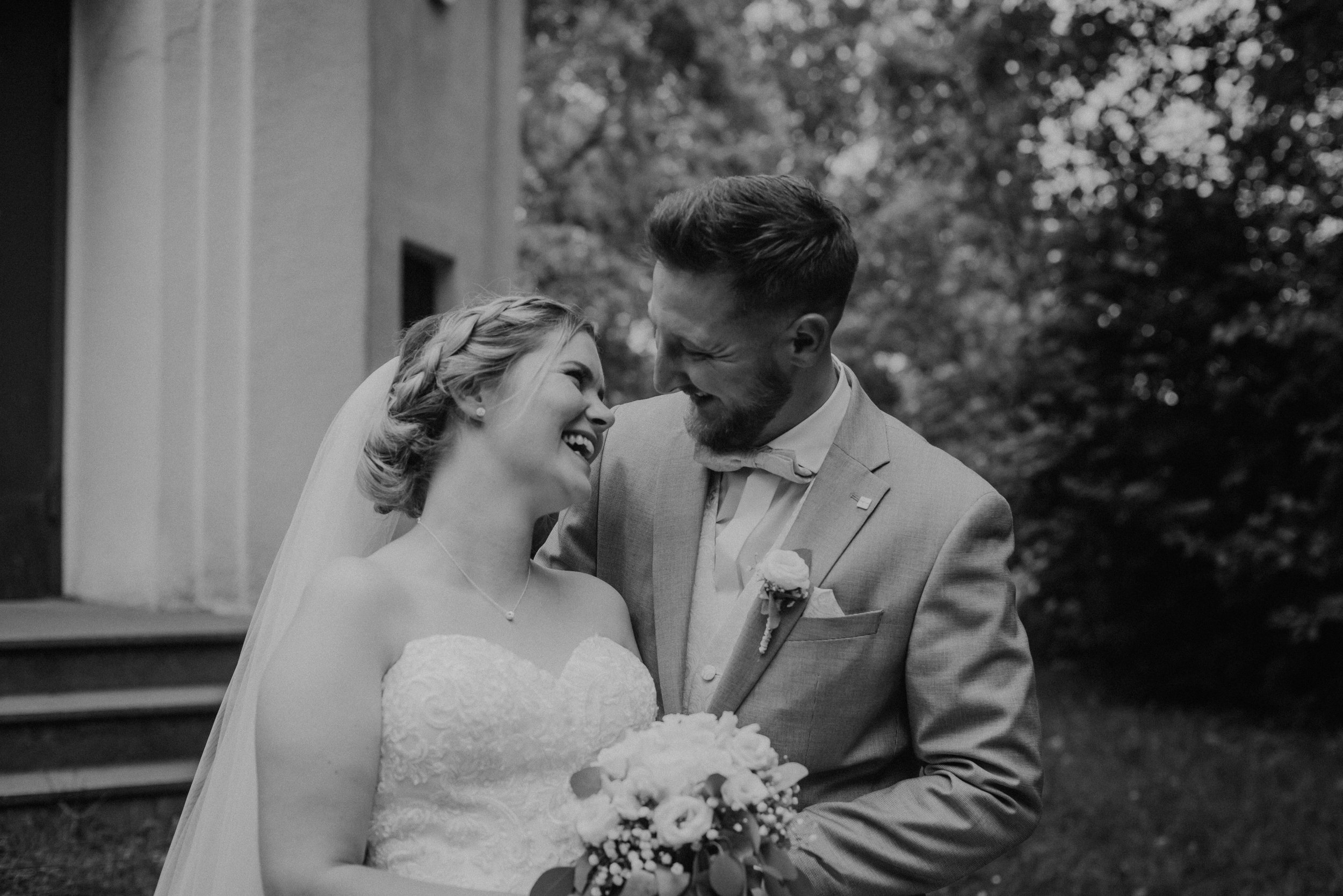 Braut und Bräutigam lachen sich an, bei ihrer Hochzeit im Freien, schwarz-weiß Foto