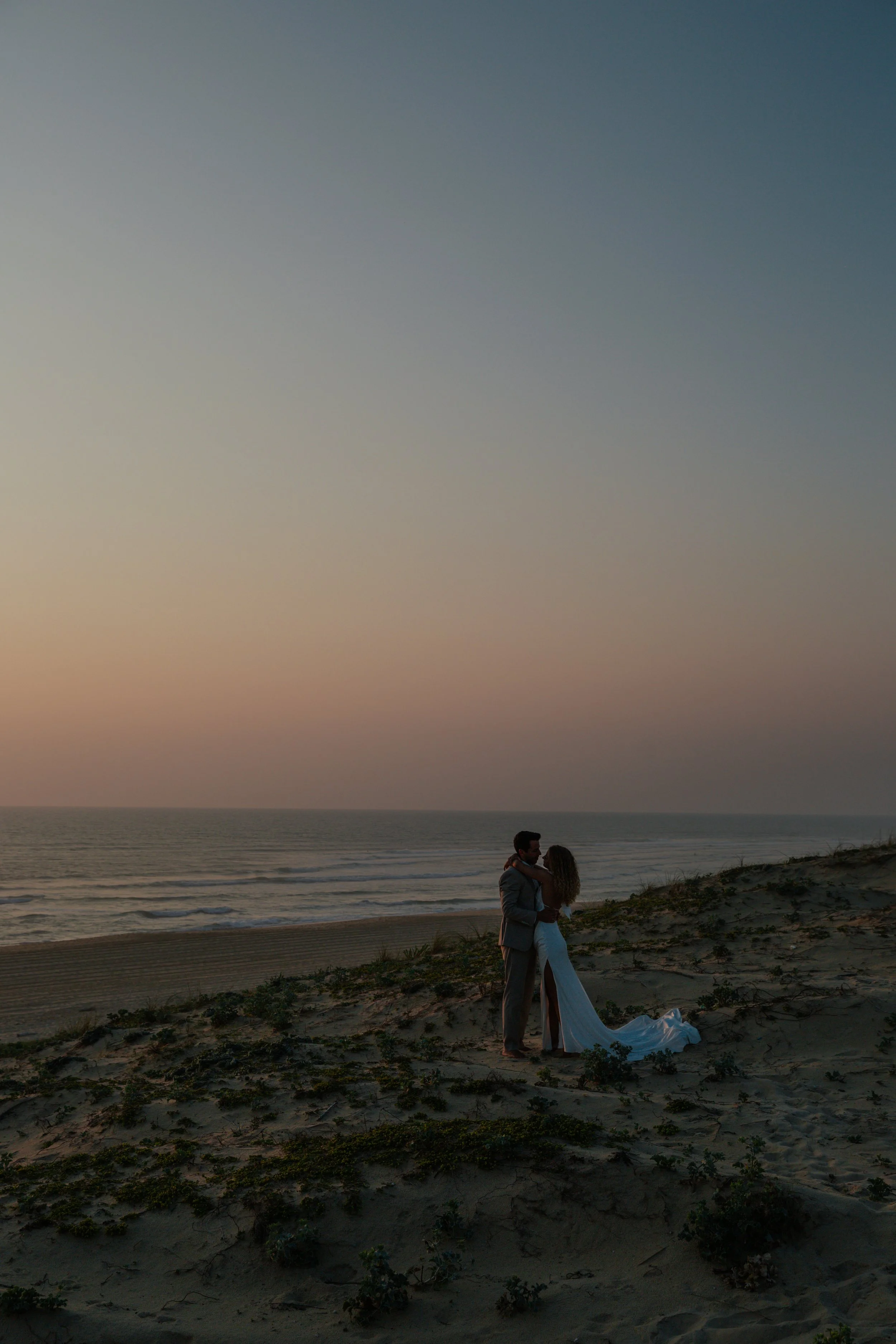 Ein Paar, das sich auf einem Sanddünenstrand bei Sonnenuntergang umarmt.