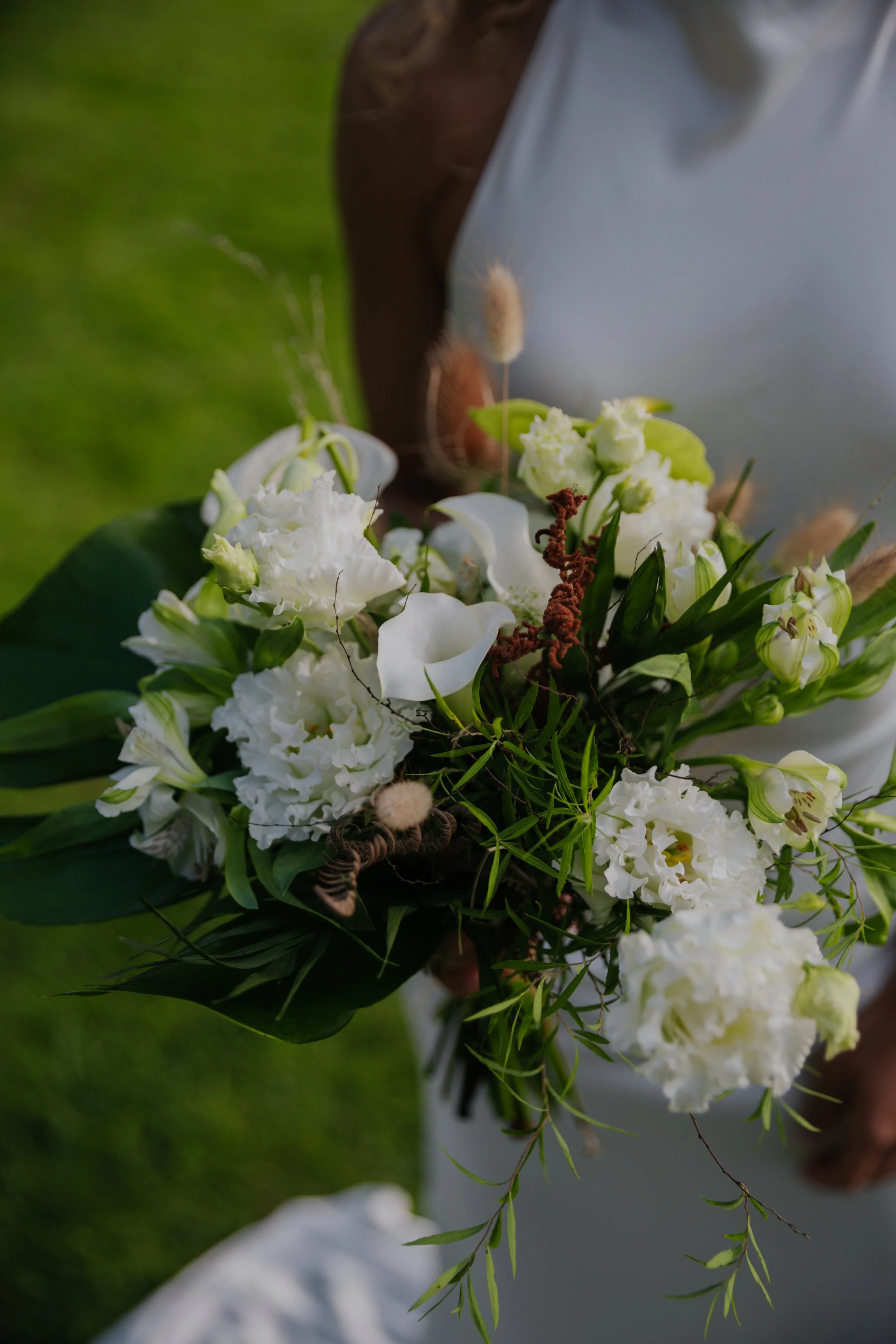 Person hält einen Blumenstrauß in weißen und grünen Farbtönen, im Hintergrund grüner Rasen.