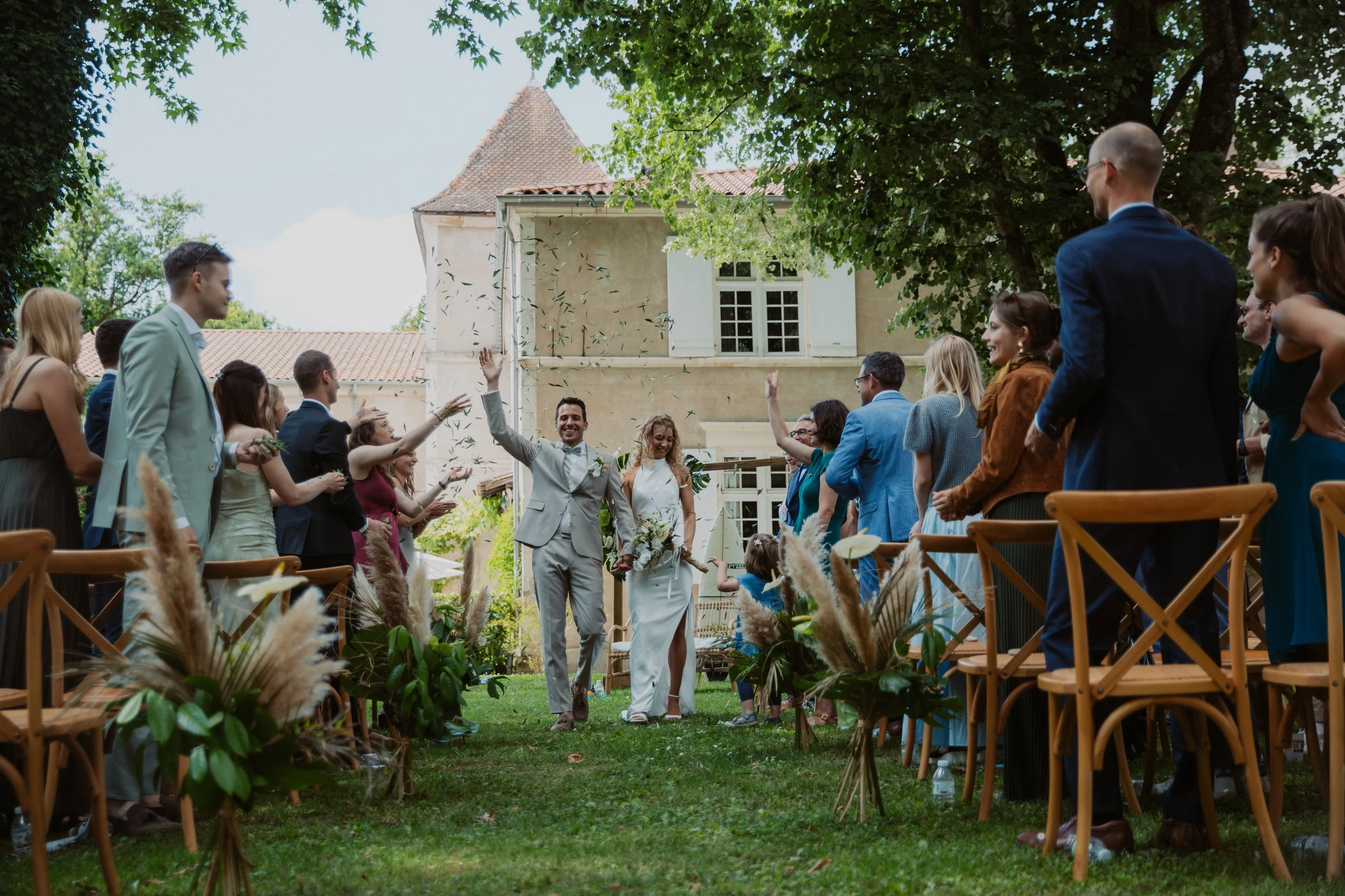 Brautpaar läuft nach Hochzeit durch einen Garten, umgeben von feiernden Freunden und Familie, während Konfetti geregnet wird.