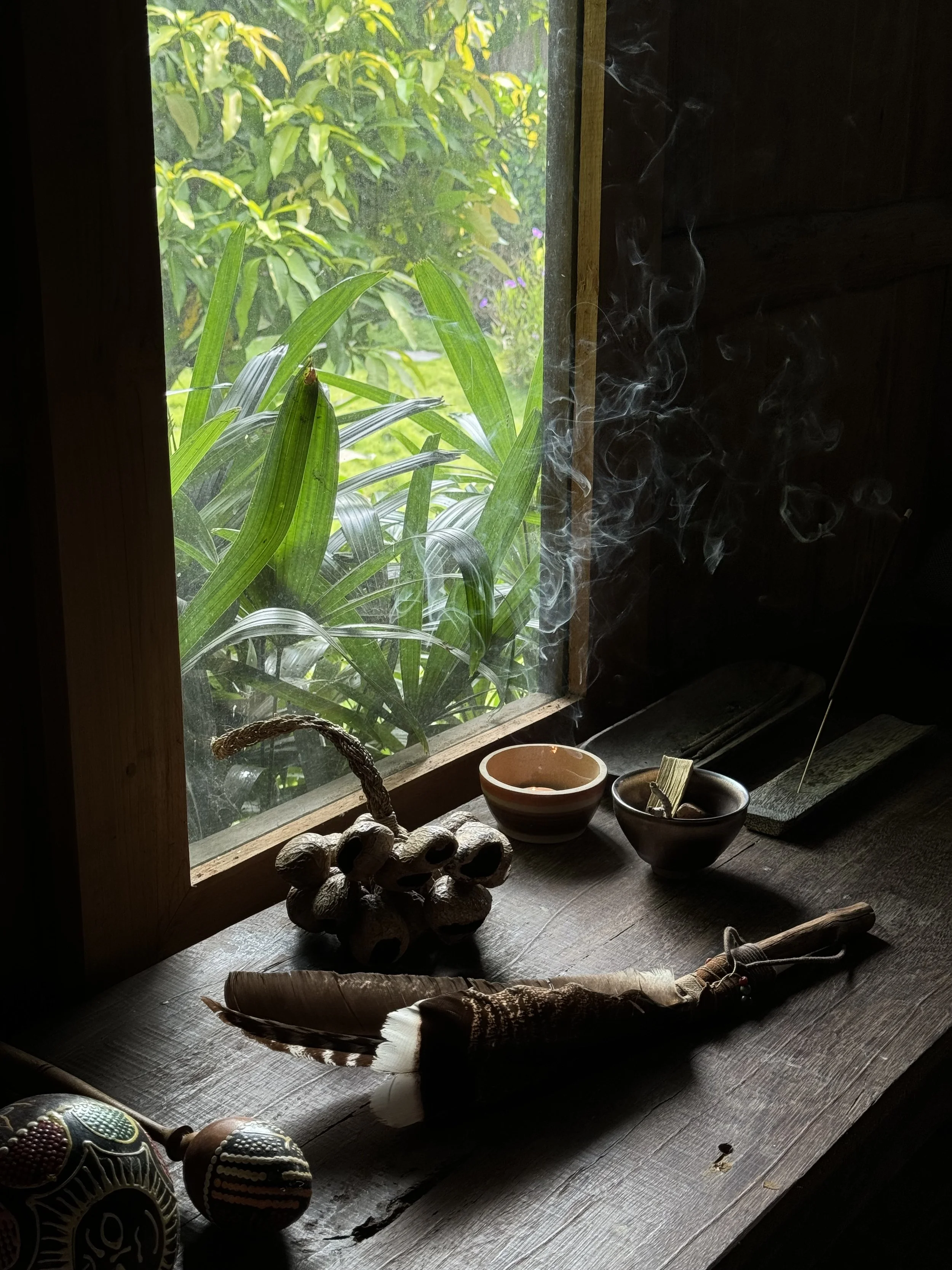 Intérieur d'une pièce avec fenêtre, objets artisanaux, deux bols, une pipe en bois avec une plume, et de la fumée qui s'élève.