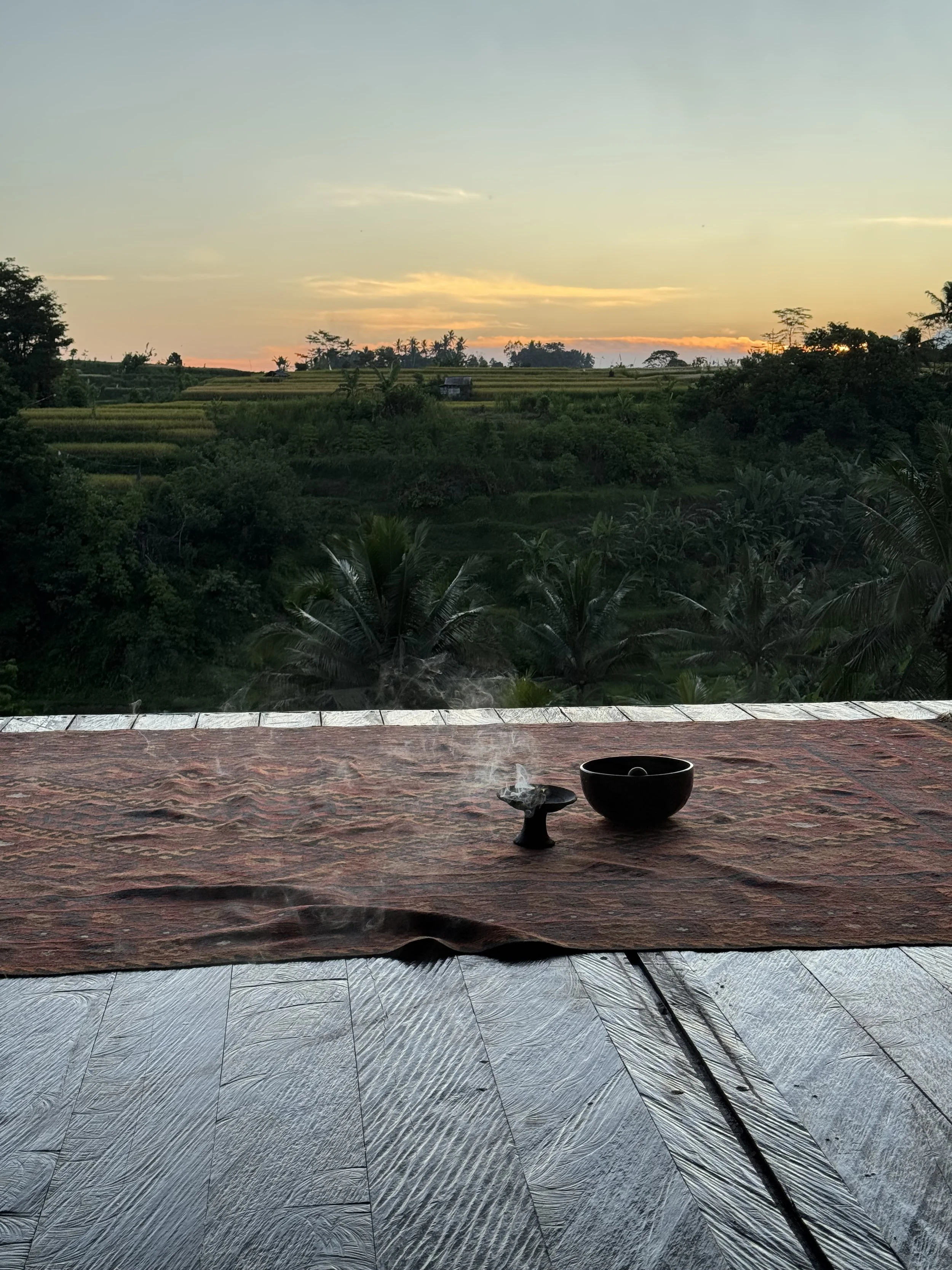 Paysage tropical avec champs verts au coucher du soleil, vue depuis une terrasse en bois avec une bol et une encensière.