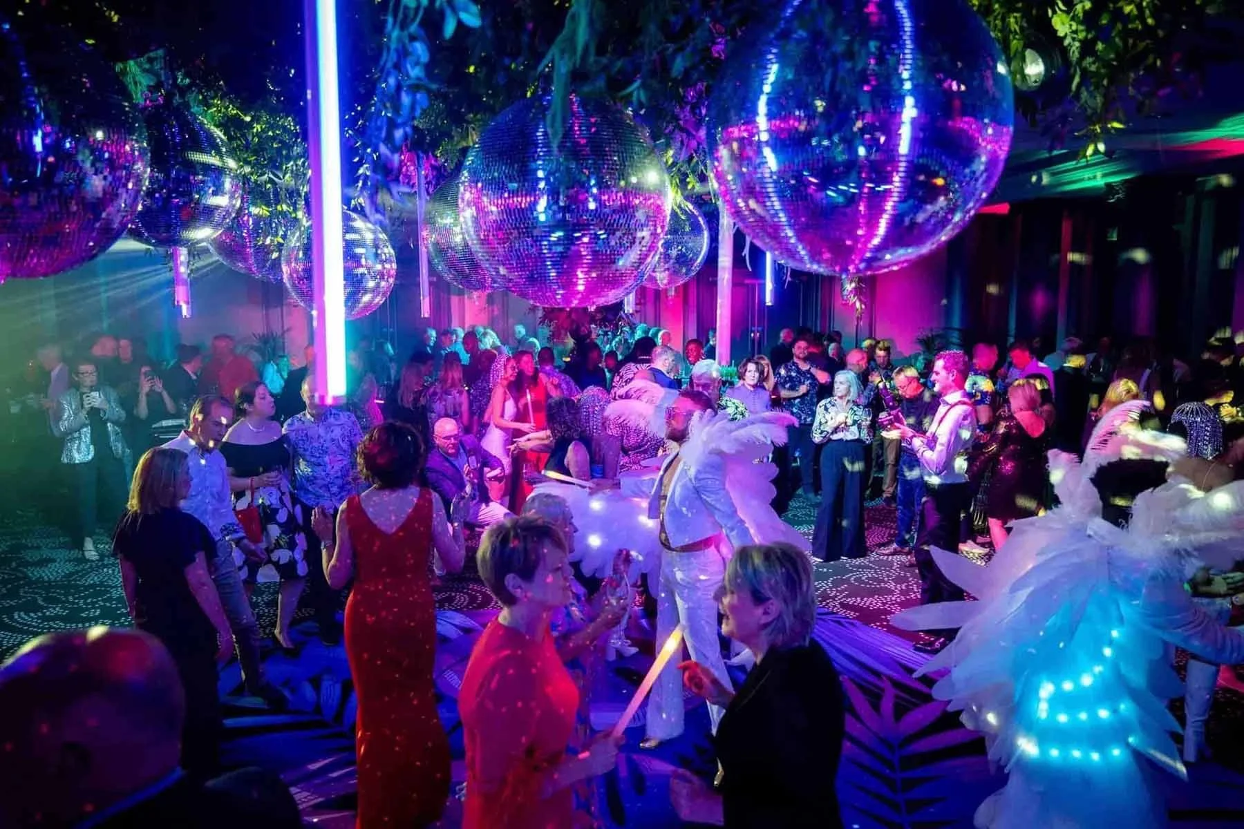 A vibrant, crowded party with disco balls, colorful lights, and people dancing in festive outfits with glowing decorations.