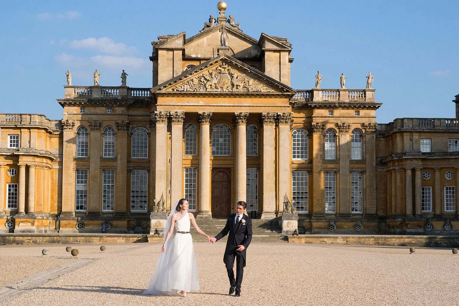 Bride and groom walking in front of a large historic building.
