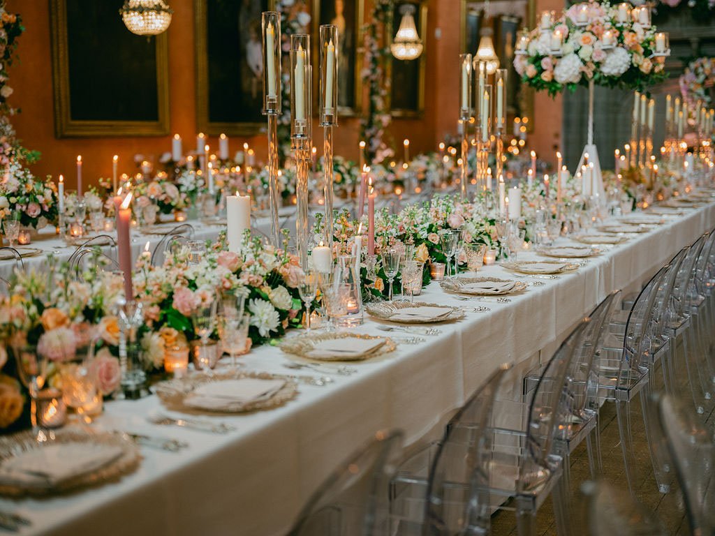 Elegant banquet table decorated with pink and white flowers, candles, and glassware, set for a formal event or wedding reception.