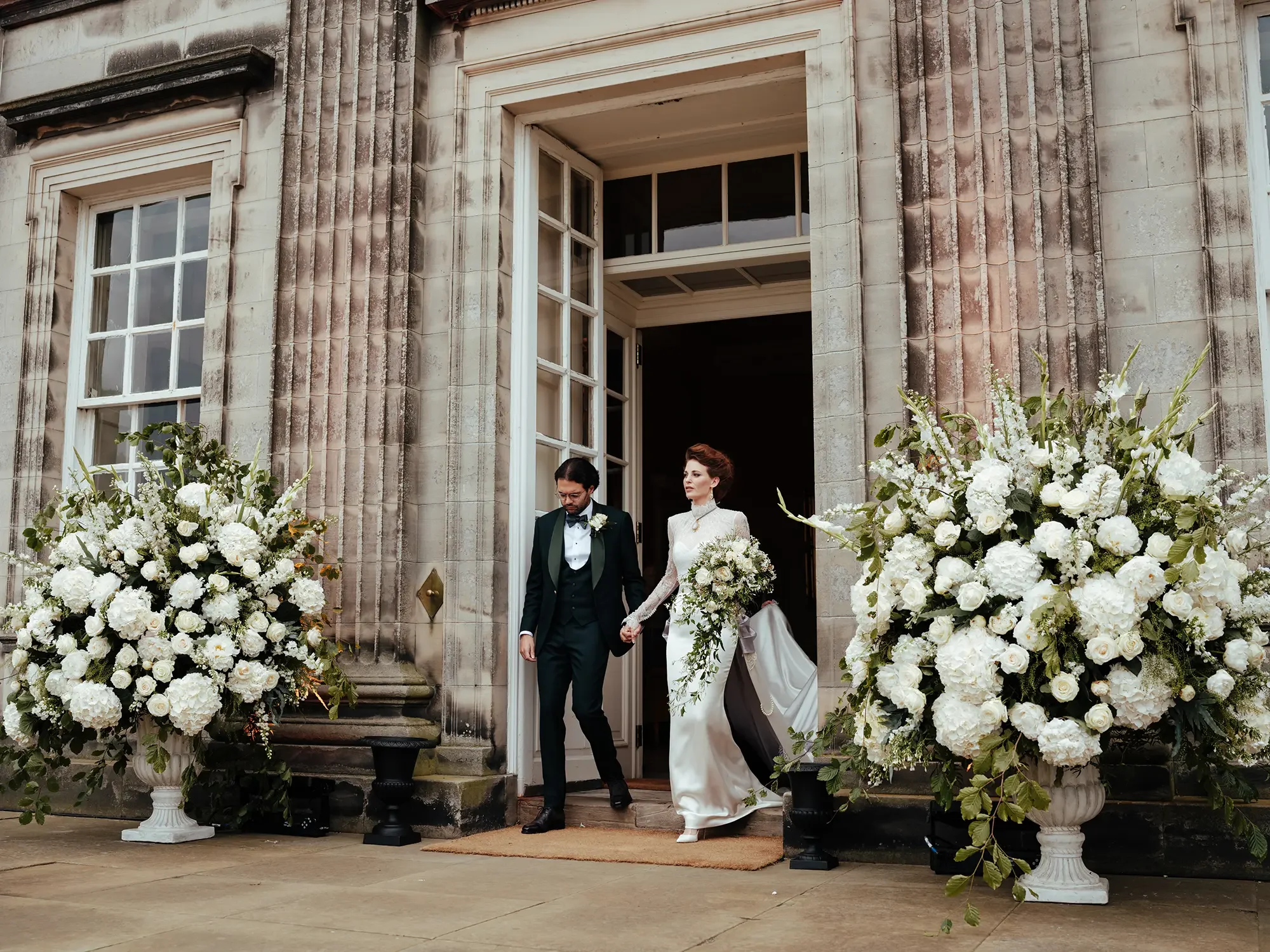 Elegant couple in wedding attire walking out of an historic building.