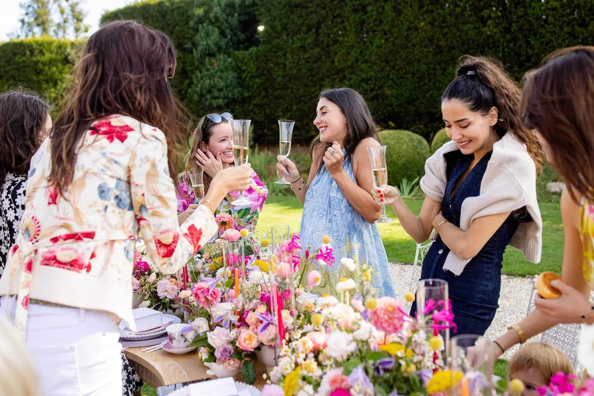 Women celebrating with champagne at an outdoor garden party with colorful flower arrangements.