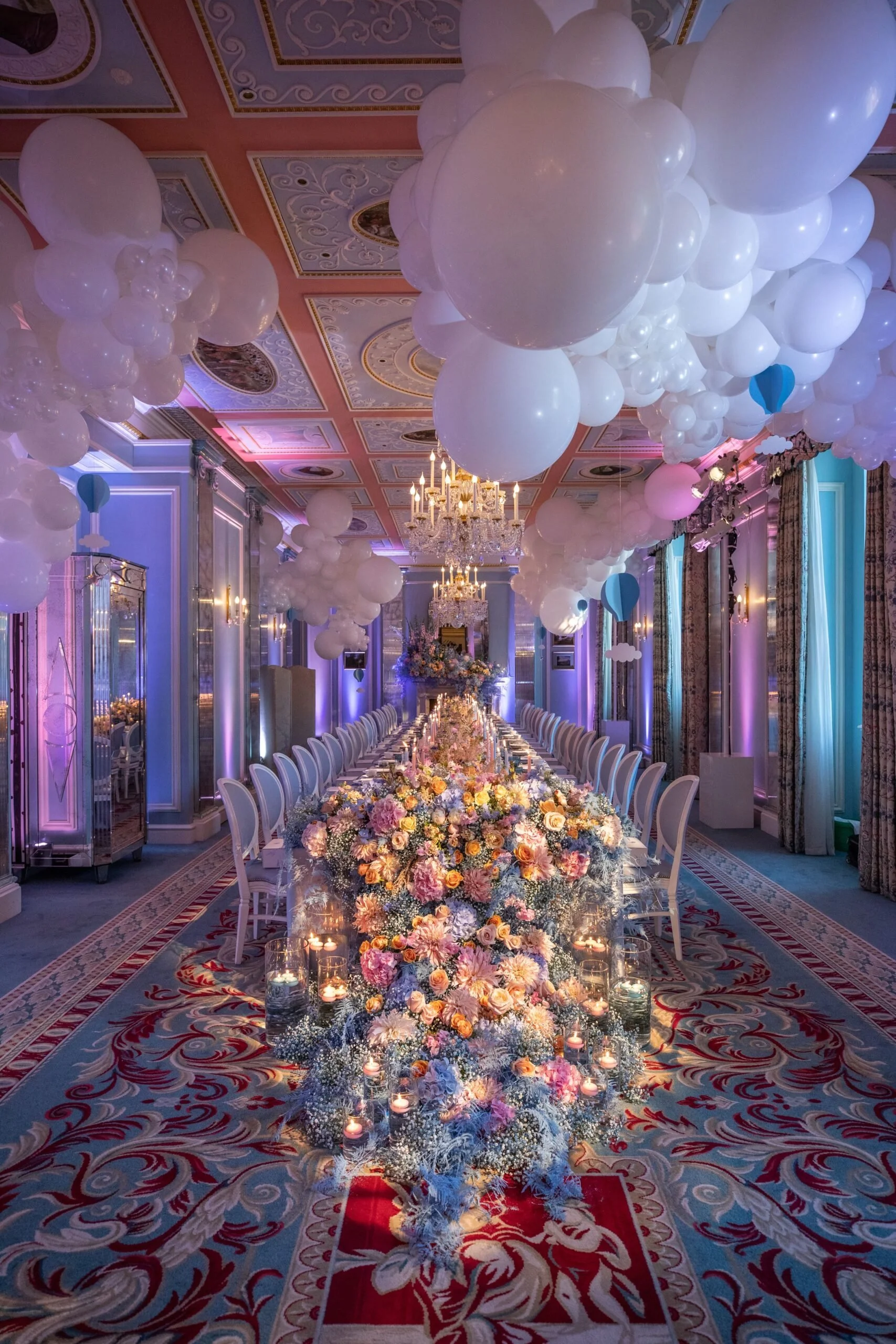 Elegant wedding reception hall decorated with white balloons, flowers, and candles, with a long table set for guests.