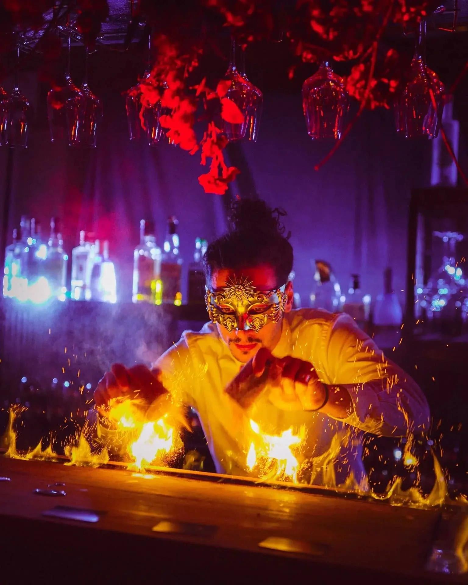 A masked bartender dazzles at an event planning showcase, performing a fiery cocktail show amid vibrant flames and glowing bottles.