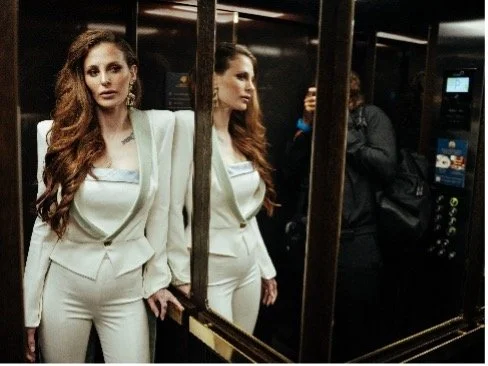 Portrait of glamorous woman leaning against a mirror wearing a white suit