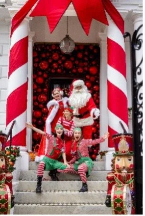 Father Christmas and joyful elves celebrate on hotel steps.