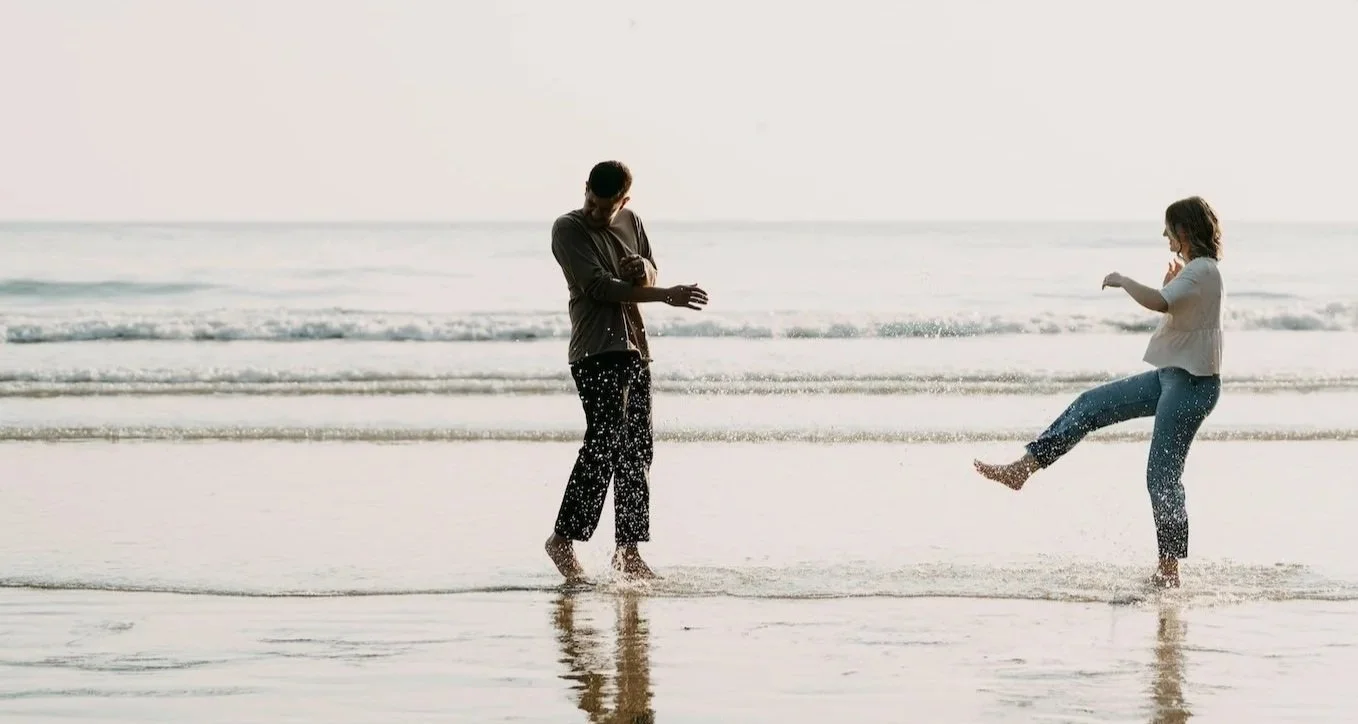 Twee mensen spelen in de zee op het strand, één man en één vrouw die water spatten.