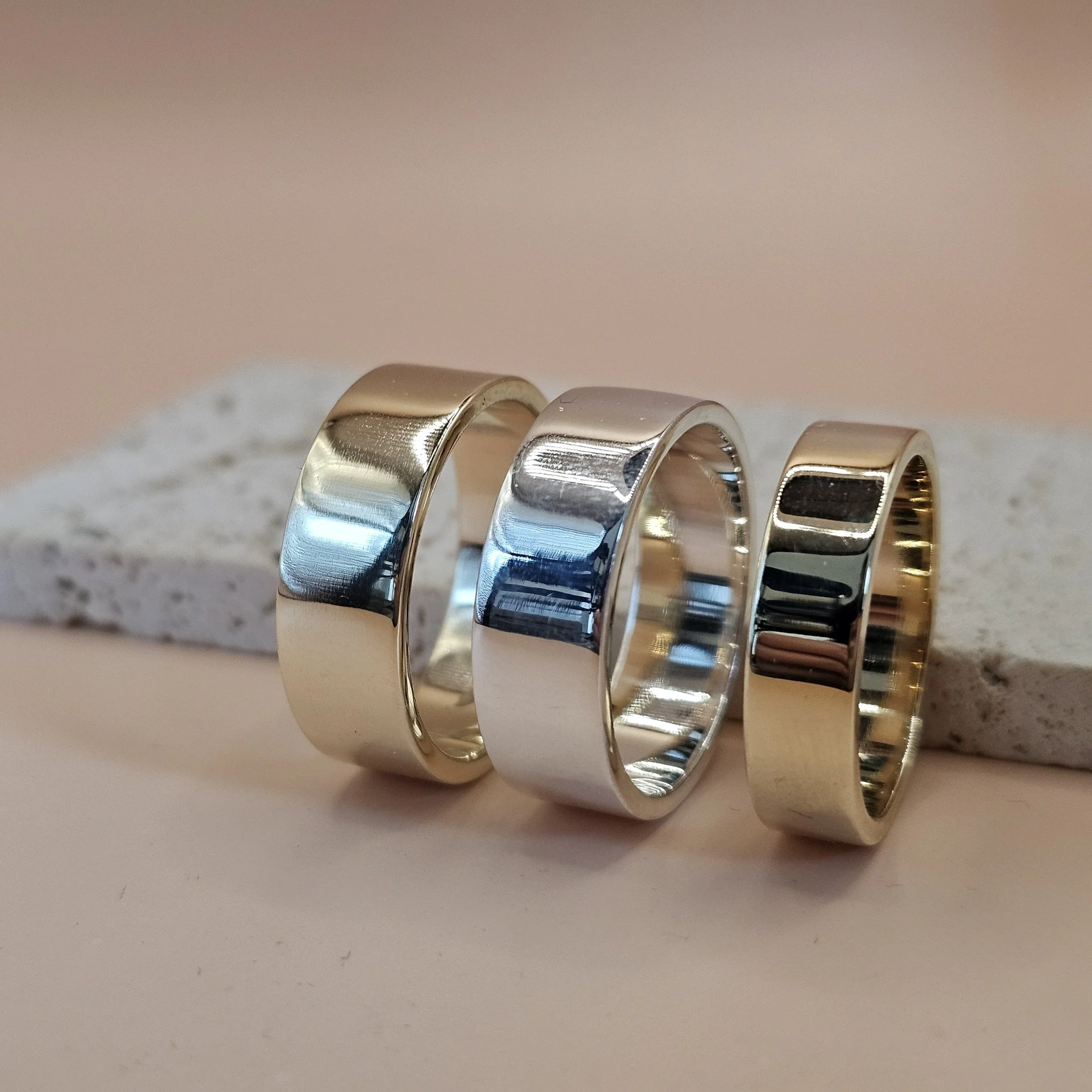 Close-up of various metallic rings, some with square or rectangular cutouts, arranged in a line on a plain surface.