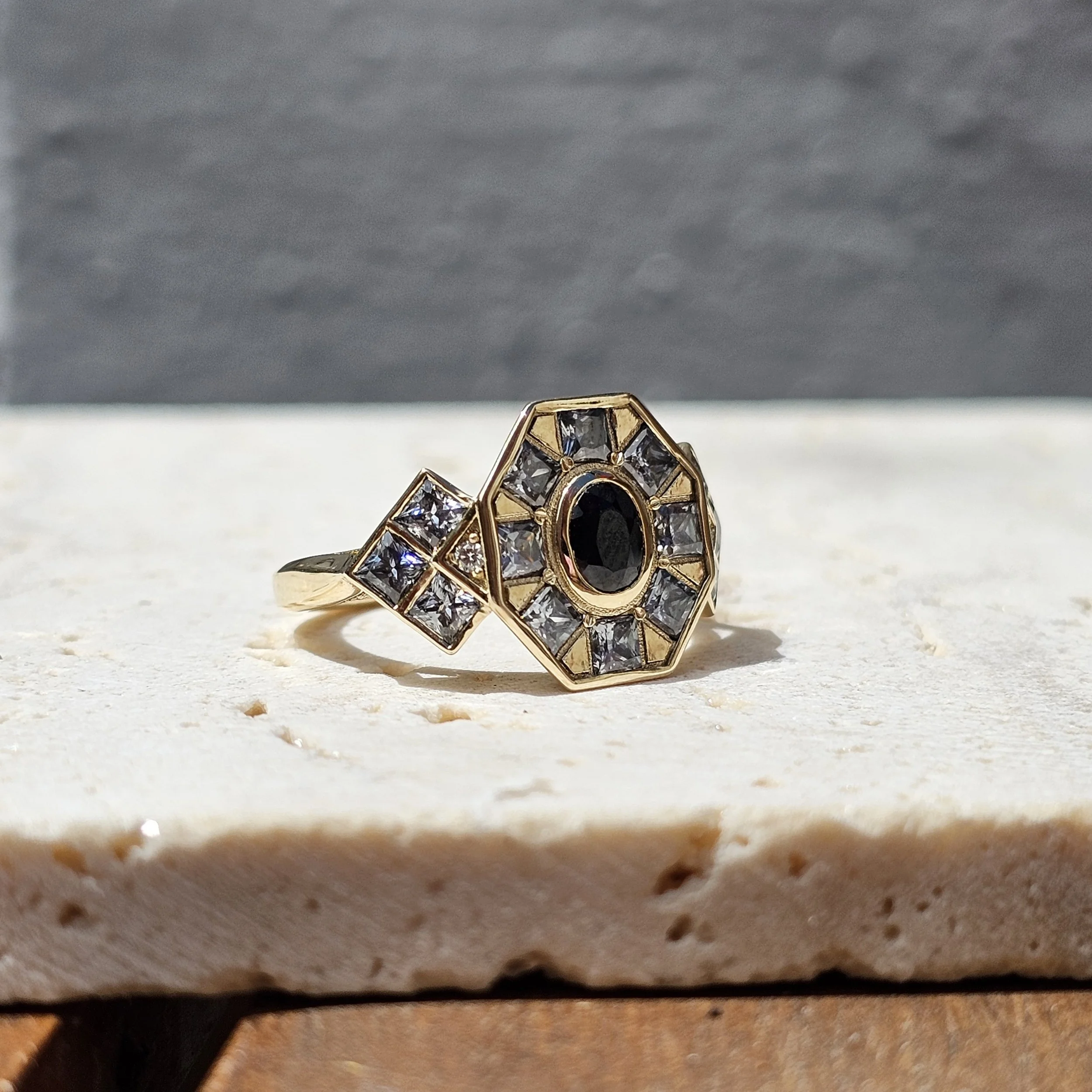 Close-up of a diamond ring with a black inner gemstone, set in a gold band, sitting on a textured surface.