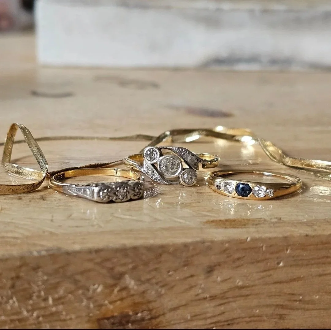 A collection of gold and silver rings with various designs and gemstones, arranged on a wooden surface.