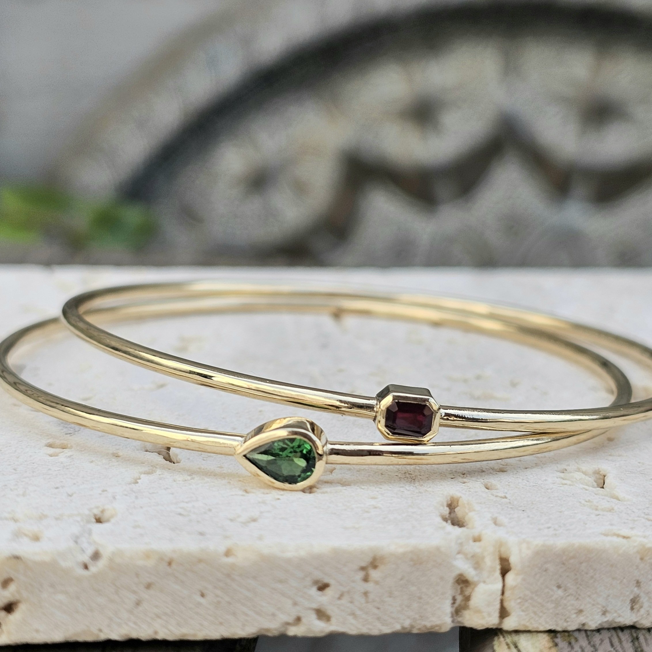 Close-up photograph of a jewelry bracelet with colored gemstones, placed on a textured surface with a blurred background.