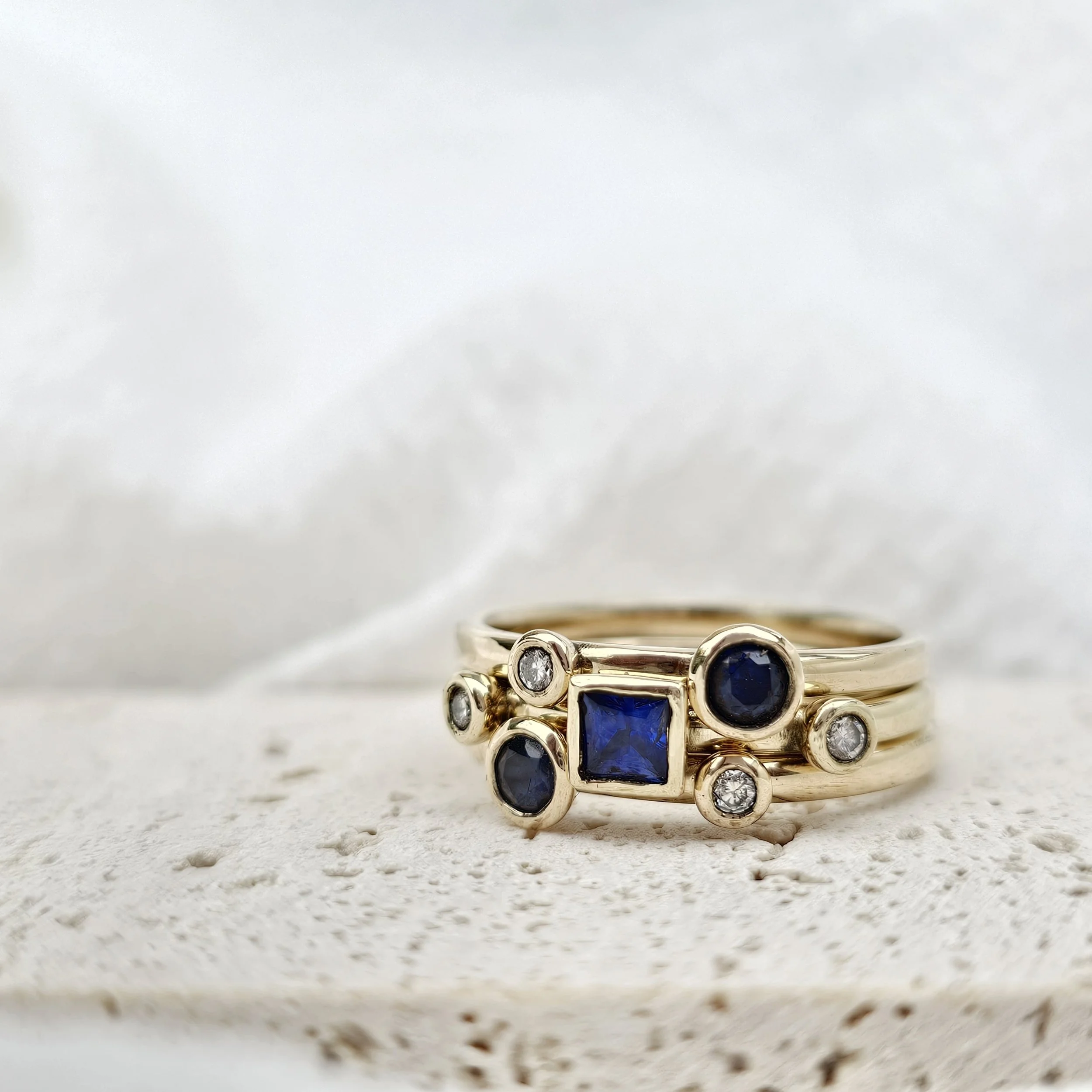 Close-up of multiple rings with gemstones, stacked together on a textured surface.