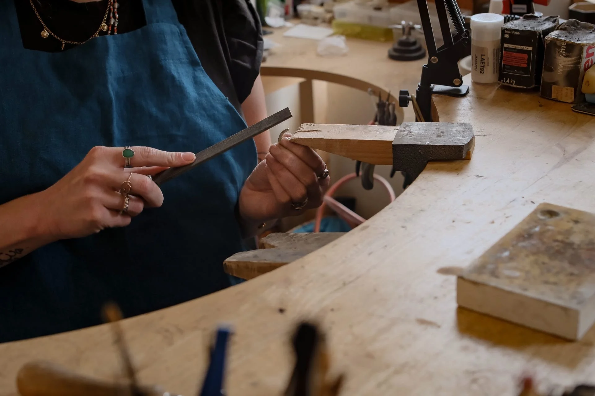 Person shaping a piece of wood with a file in a woodworking workshop.
