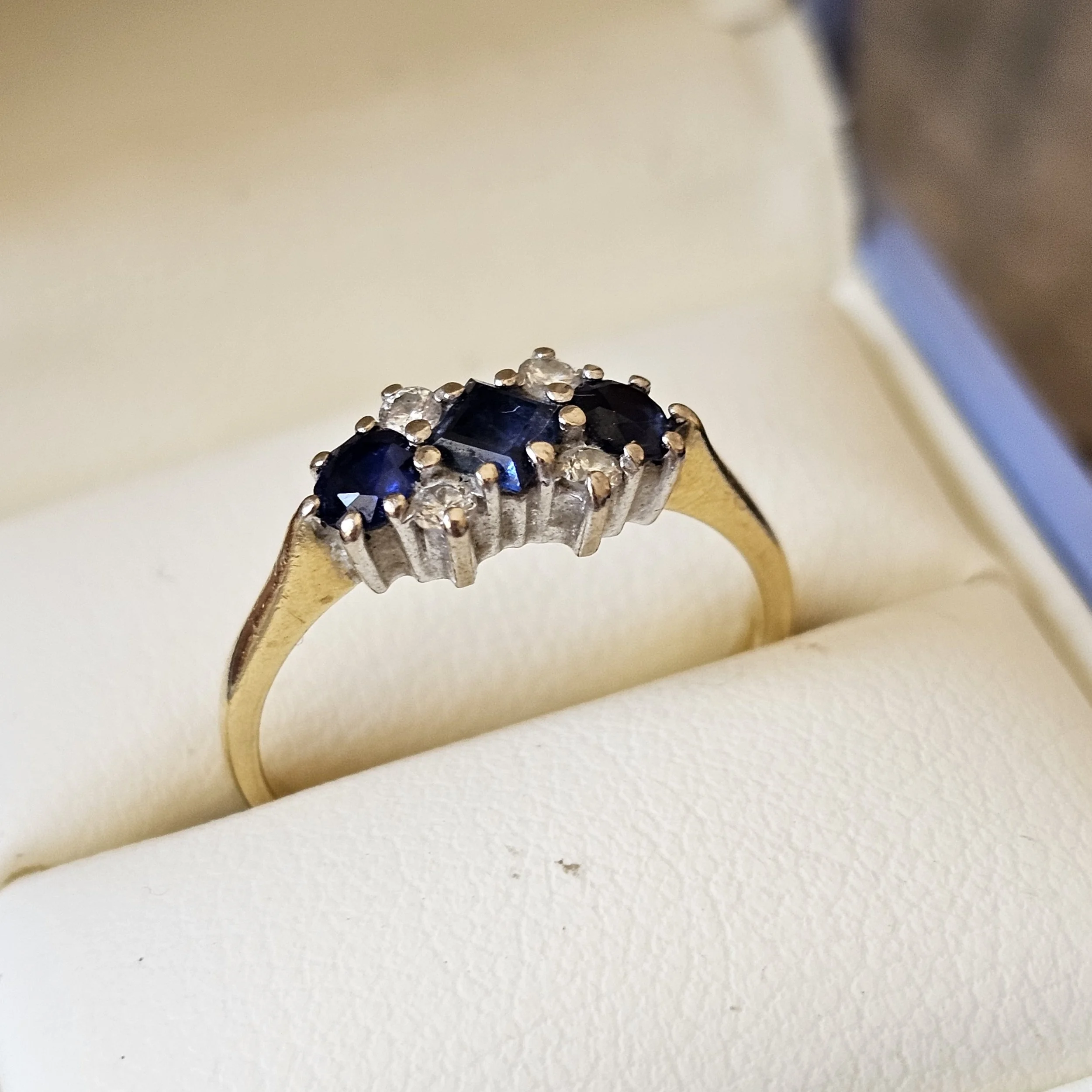 Close-up of a ring with dark blue gemstones and small clear stones set in a silver band.