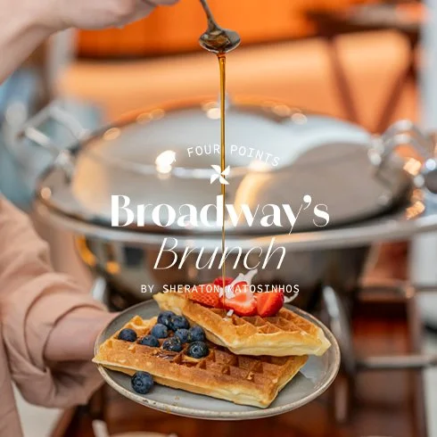 Panqueca com morangos e mirtilos, com xarope sendo vertido por cima, em um café da manhã estilo brunch.