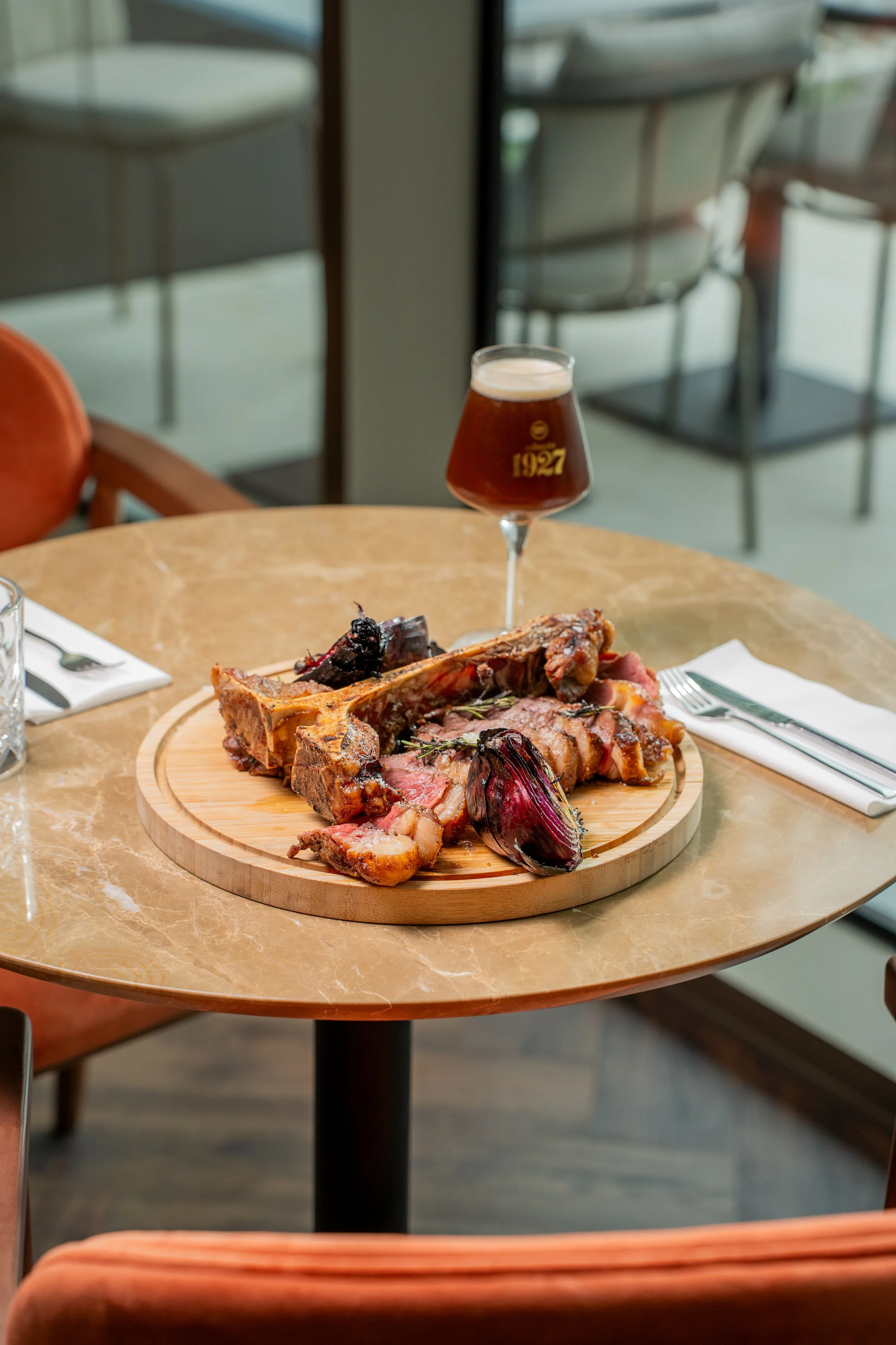 Prato de carne assada com osso e cebola roxa, acompanhado de cerveja artesanal escura, em um restaurante