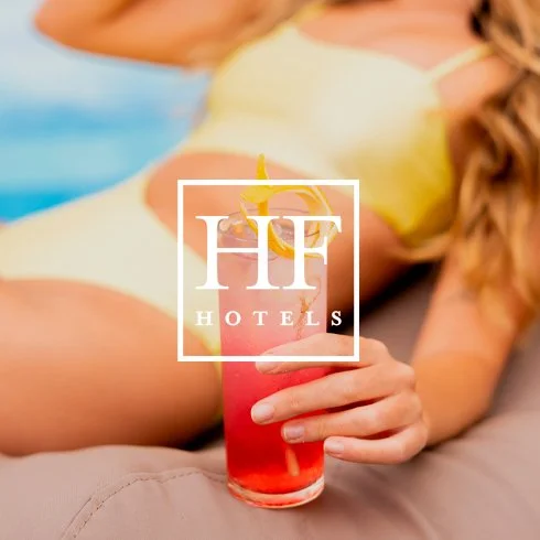 Pessoa deitada na praia segurando um drink rosa com limão e guarda-chuva de papel, com logo de hotel sobre a imagem.