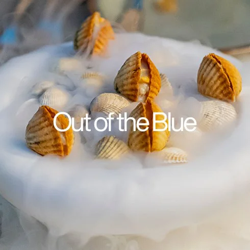 Dois sorvetes com cobertura de chantilly e confeitos, decorados com conchas de sorvete, com a frase 'Out of the Blue' em destaque.