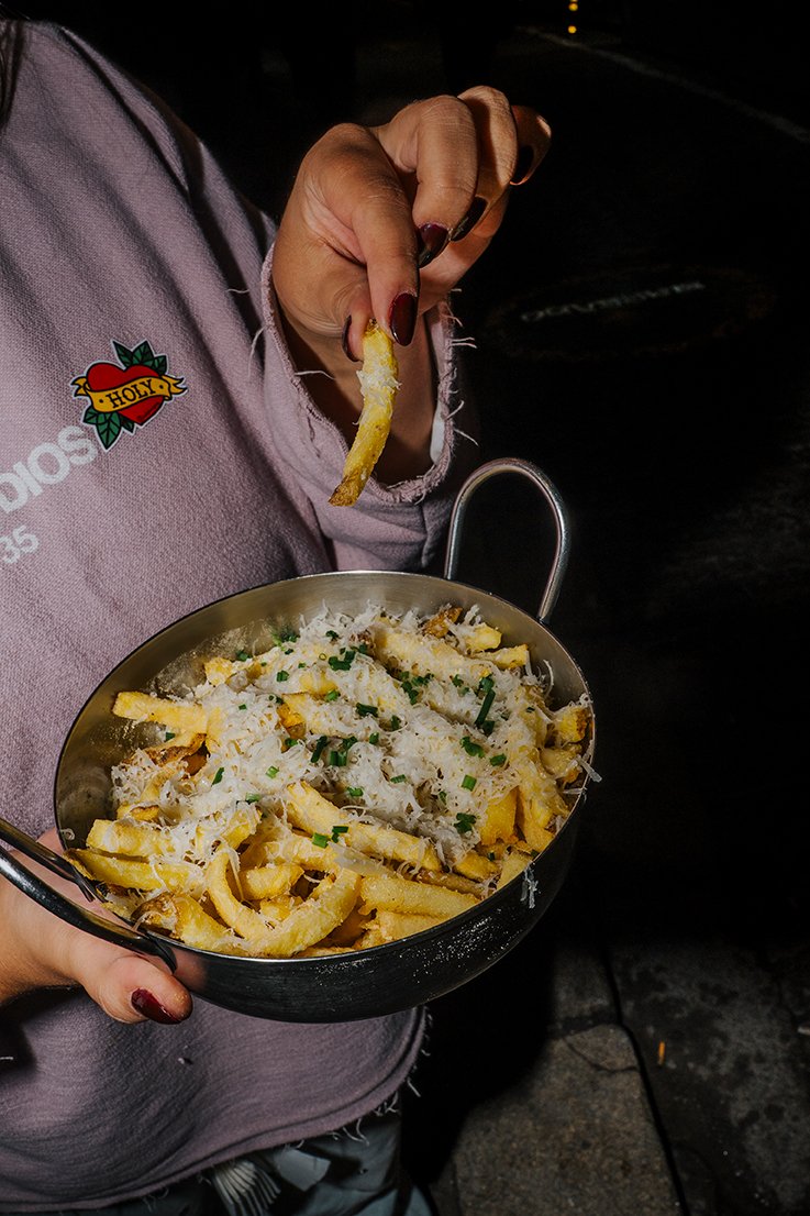 Pessoa segurando uma tigela de macarrão com queijo ralado, cebolinha e uma fatia de limão, vestindo uma blusa rosa com uma tatuagem no braço.