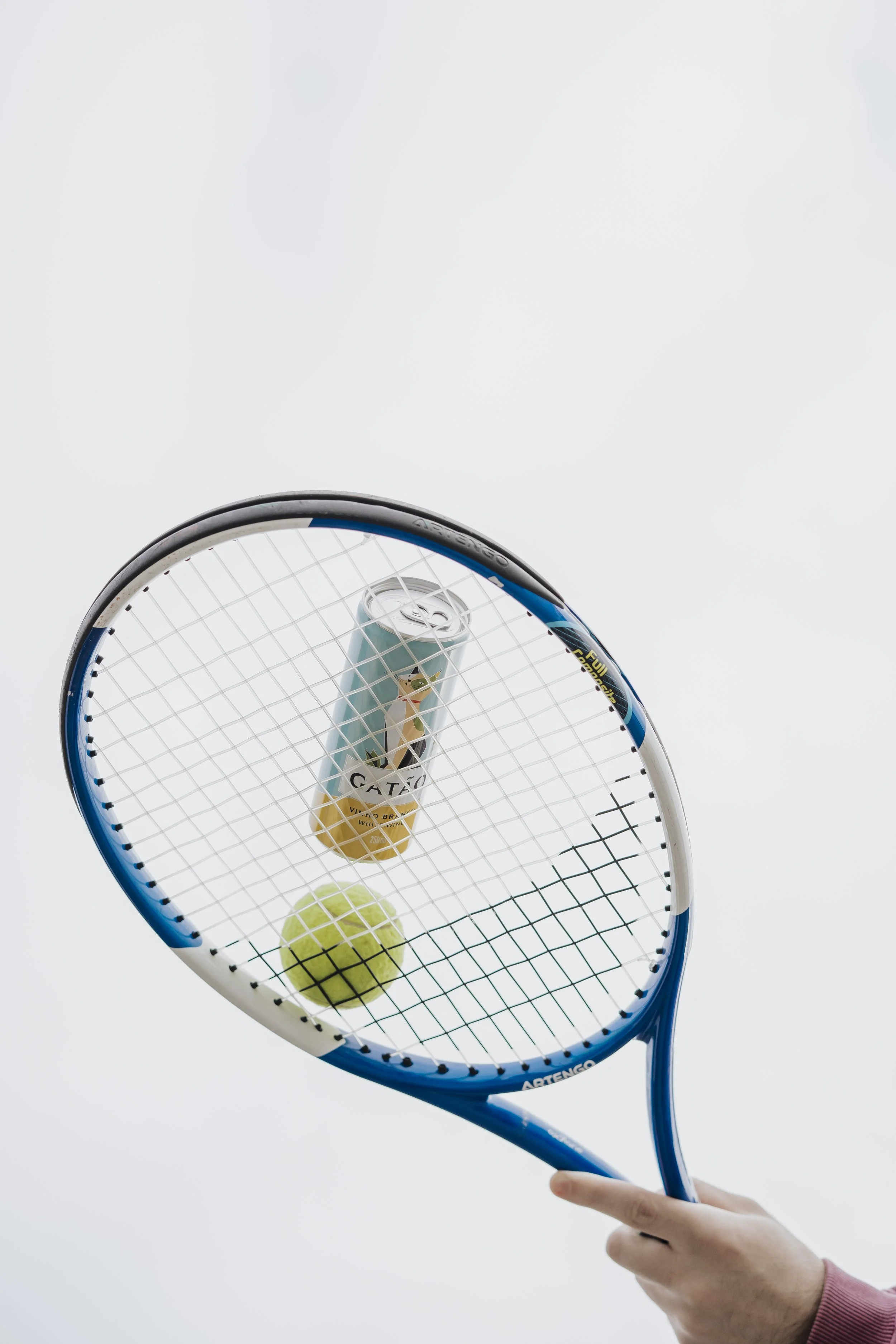 Raquete de tênis, bola de tênis, lata de suco vista de baixo, contra um céu nublado.