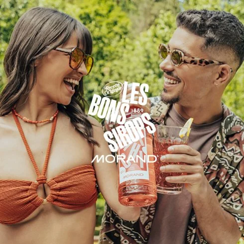 Um casal sorridente se divertindo ao ar livre, segurando uma jarra de drink rosa em um dia ensolarado.