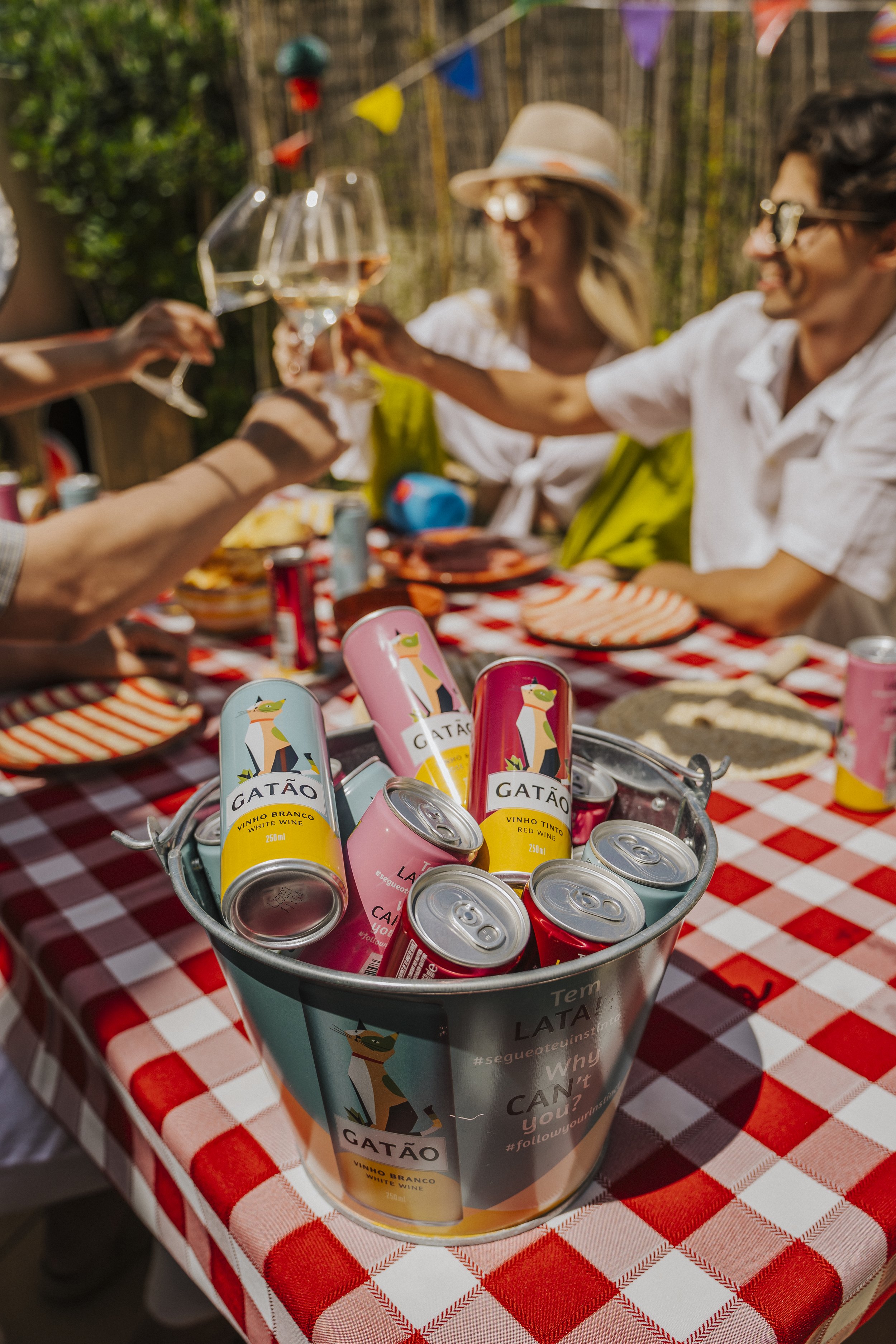 Pote de baldes de bebidas na mesa com pessoas brindando ao fundo.