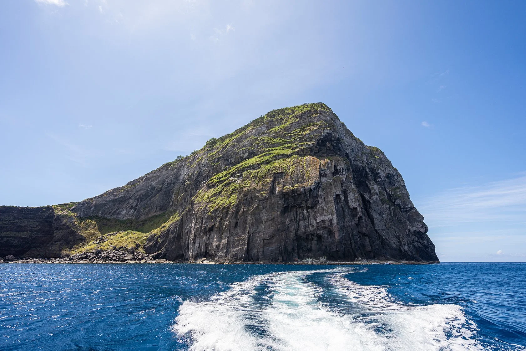 Ilha rochosa com vegetação e mar ao fundo.